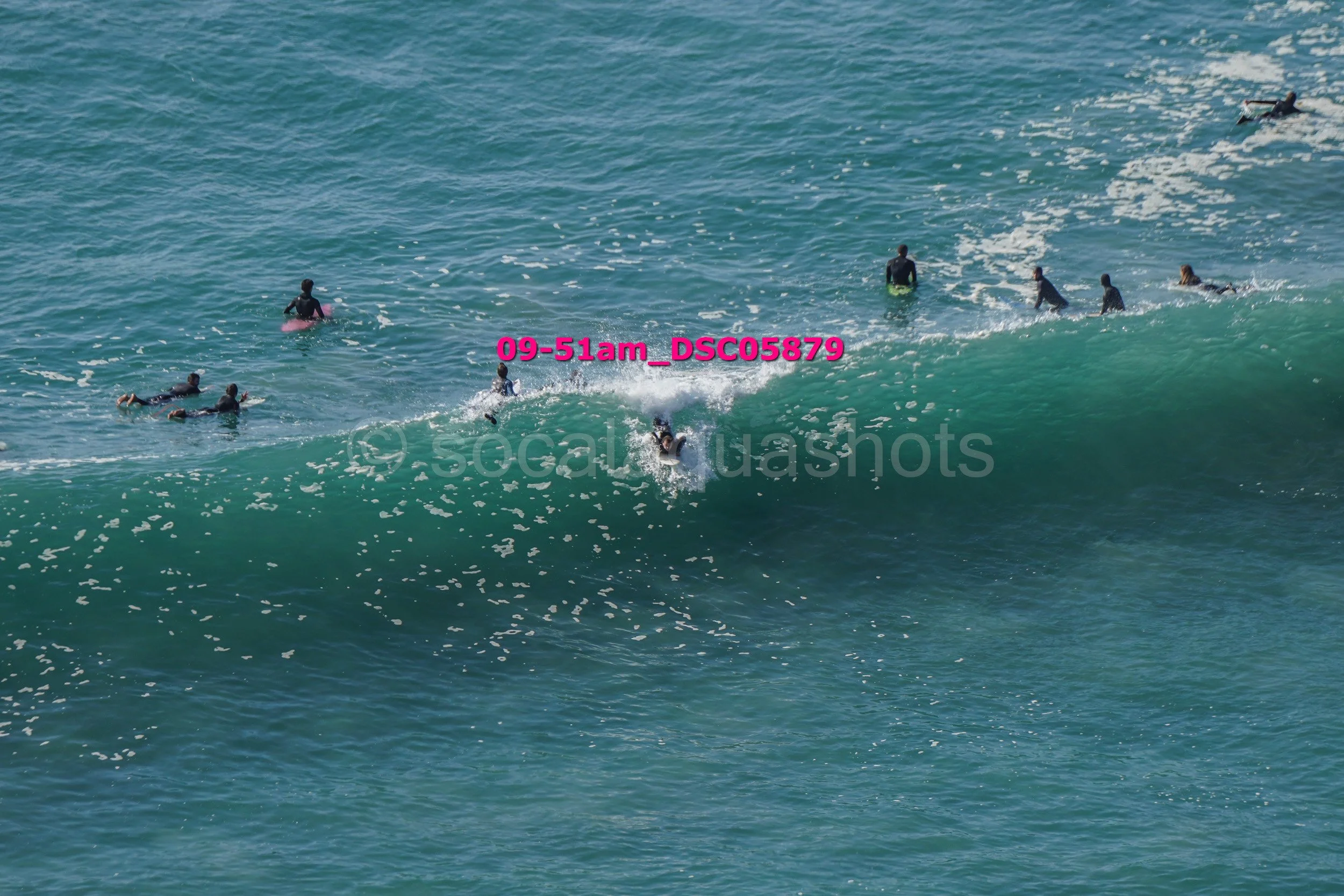 Surfers riding a large wave in the ocean with some surfers paddling on their surfboards nearby.