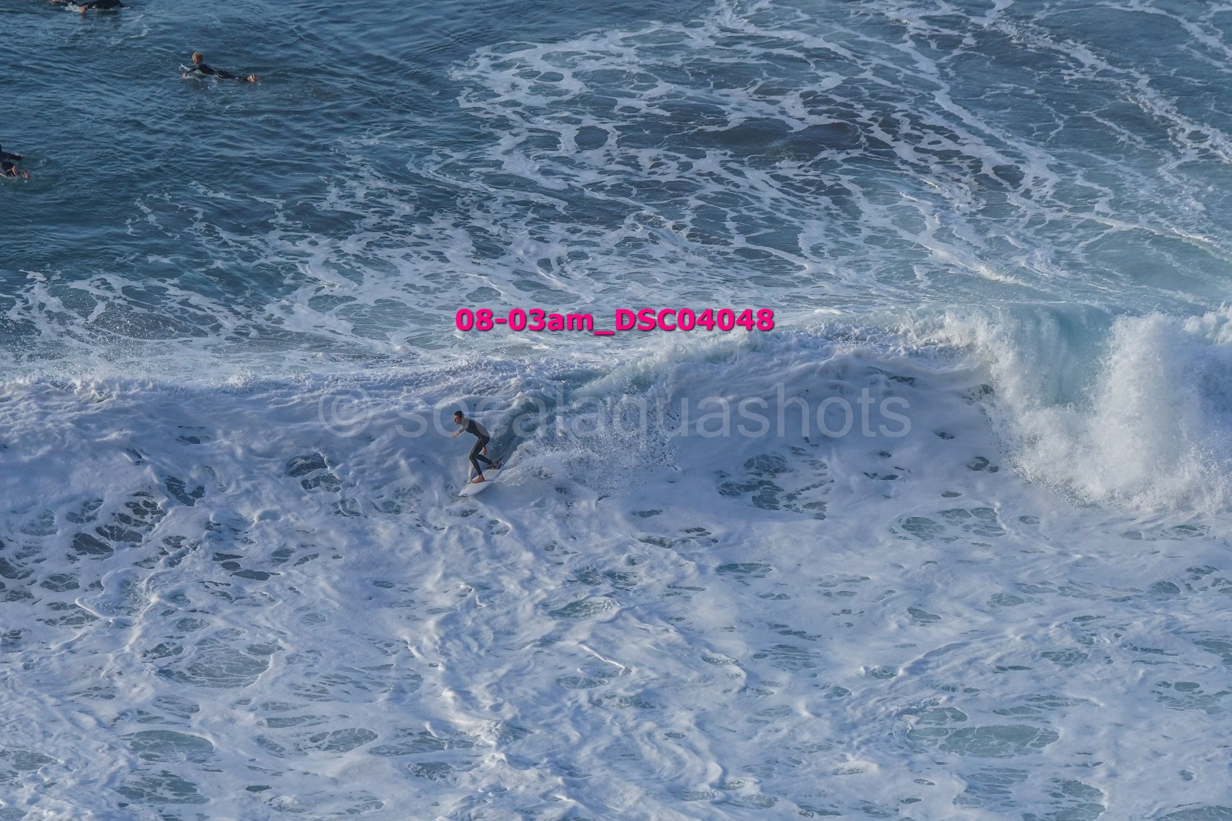 Surfer riding a wave in the ocean with two other surfers swimming nearby.