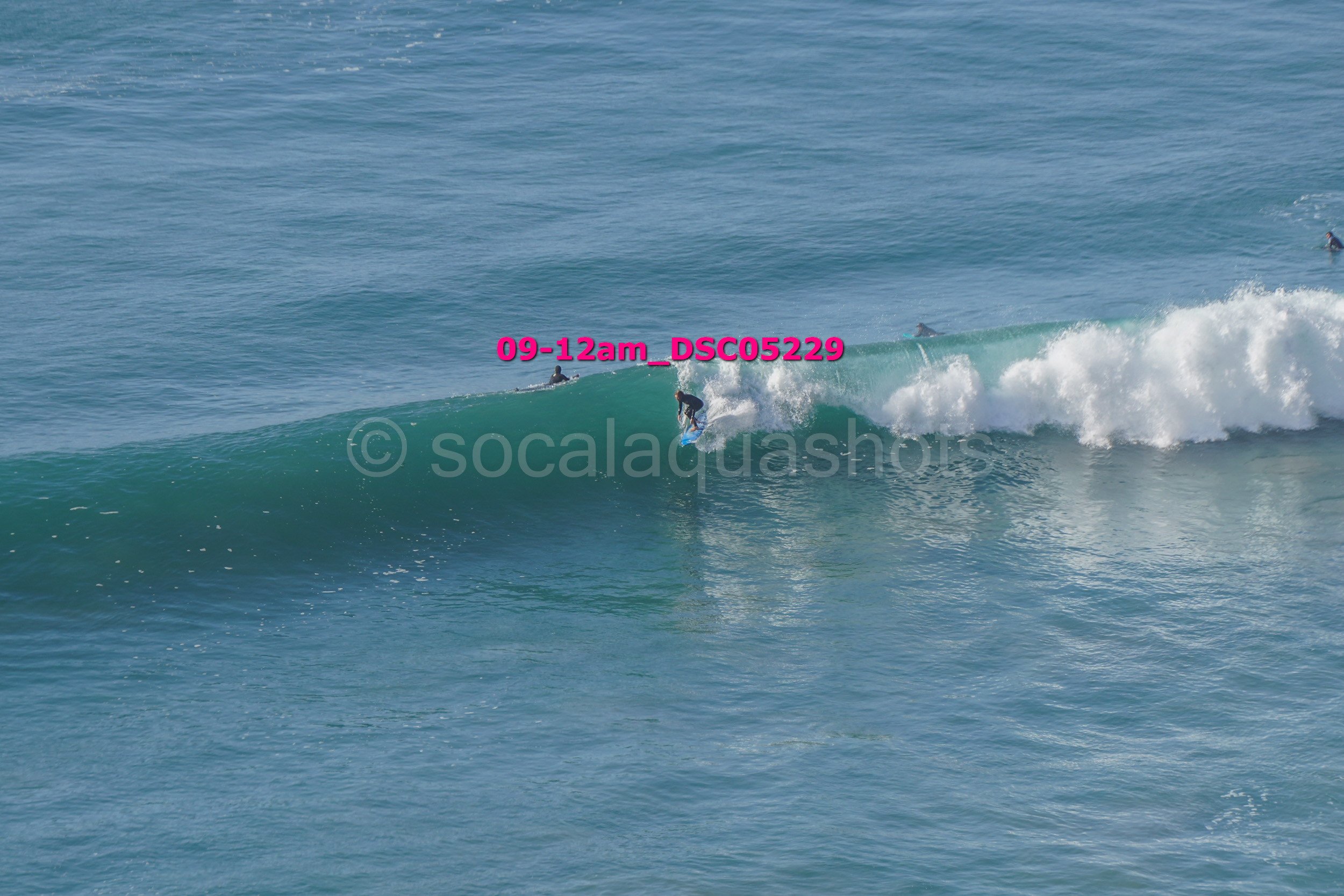 A surfer riding a wave in the ocean with several other surfers in the water surrounding him.