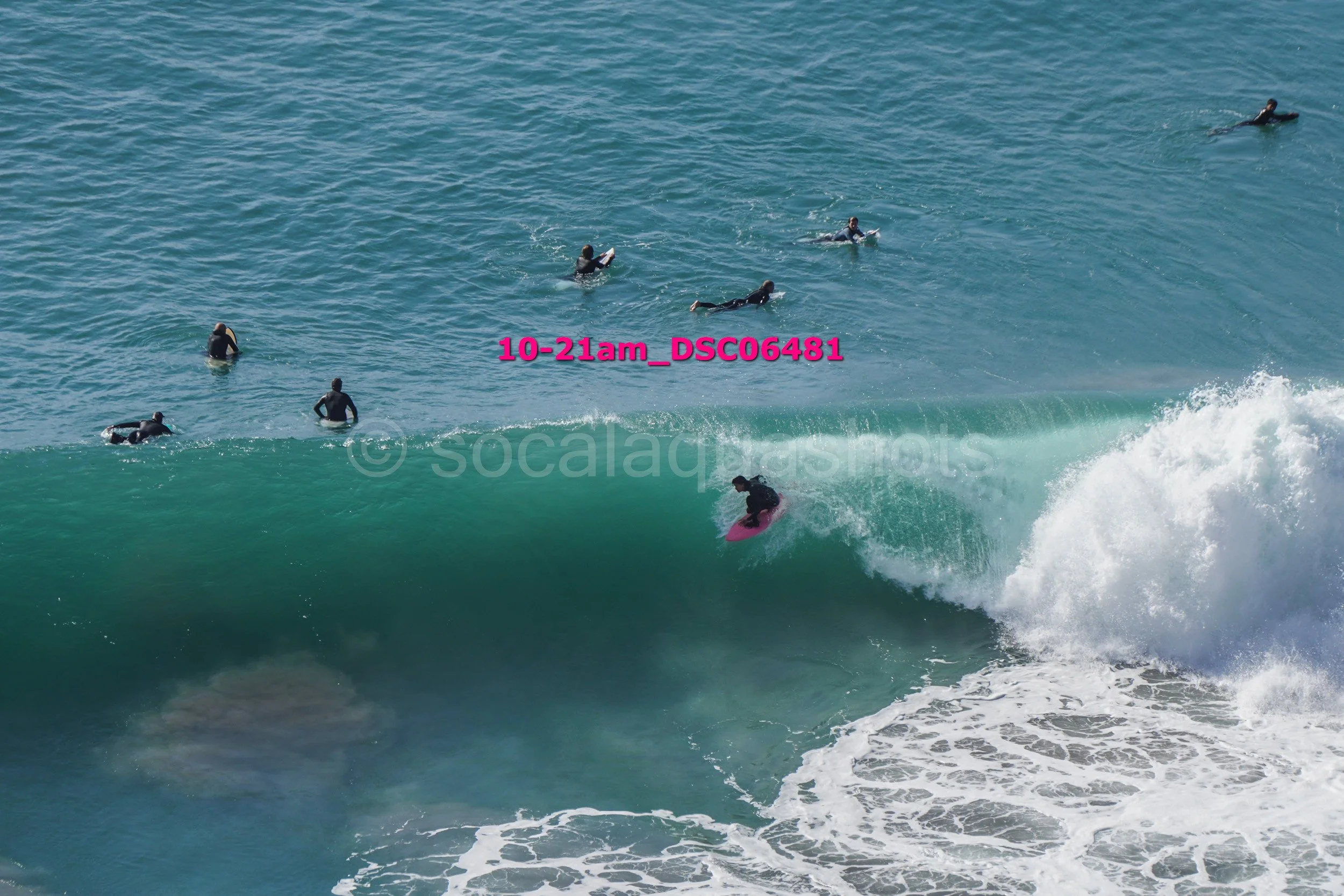 Surfer riding a wave while several people swim in the ocean in the background.