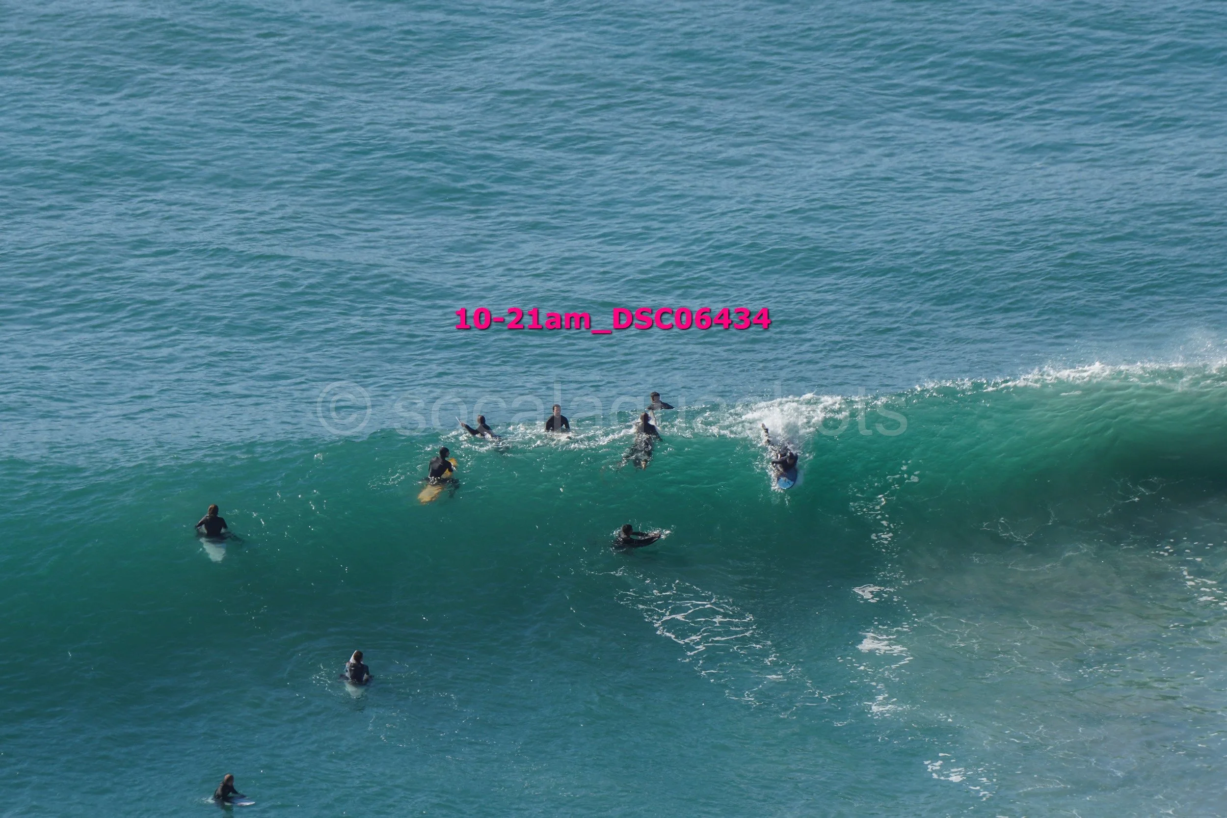 People surfing in the ocean, with some riding a wave and others paddling.