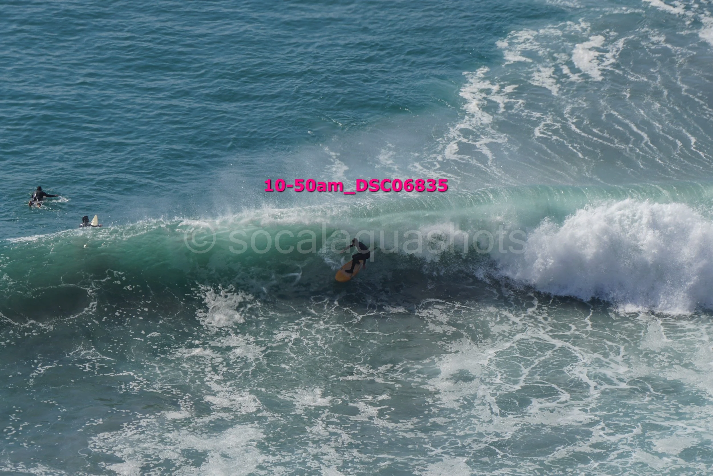 Surfer riding a wave with three other surfers nearby in the ocean during daylight.