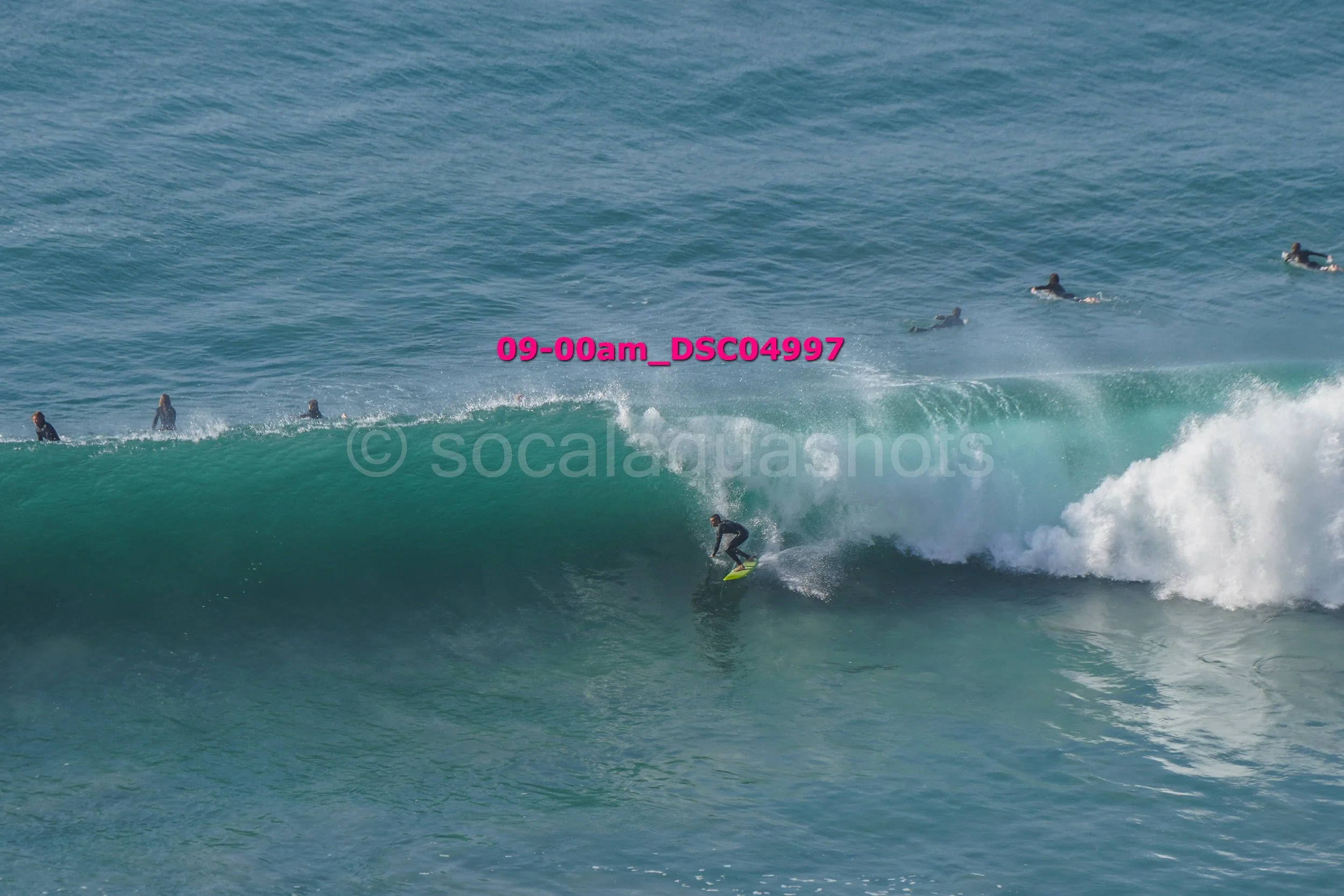 A surfer riding a wave with several surfers in the water watching.