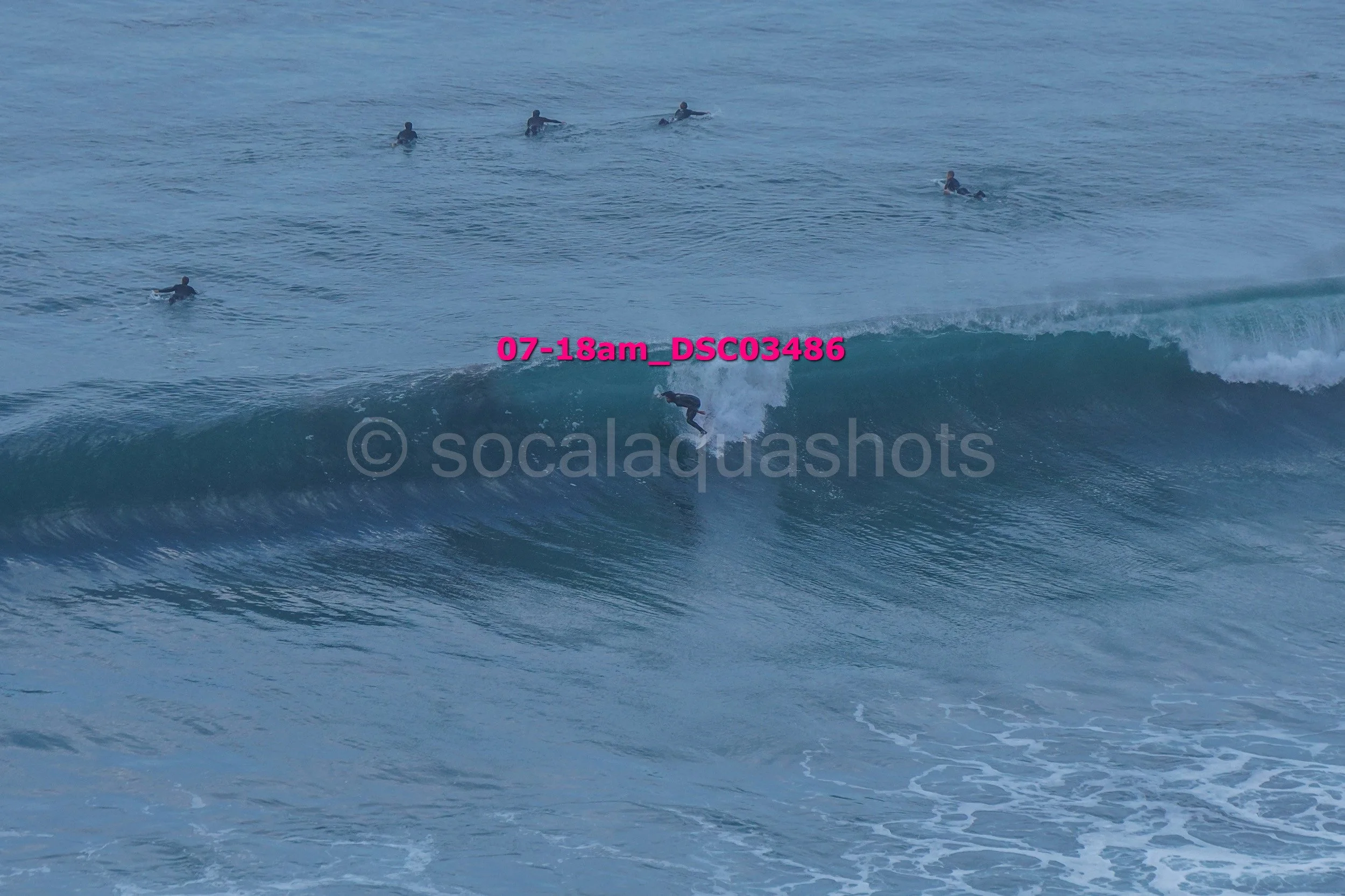 Surfer riding a wave at the beach with several other surfers in the water in the background.
