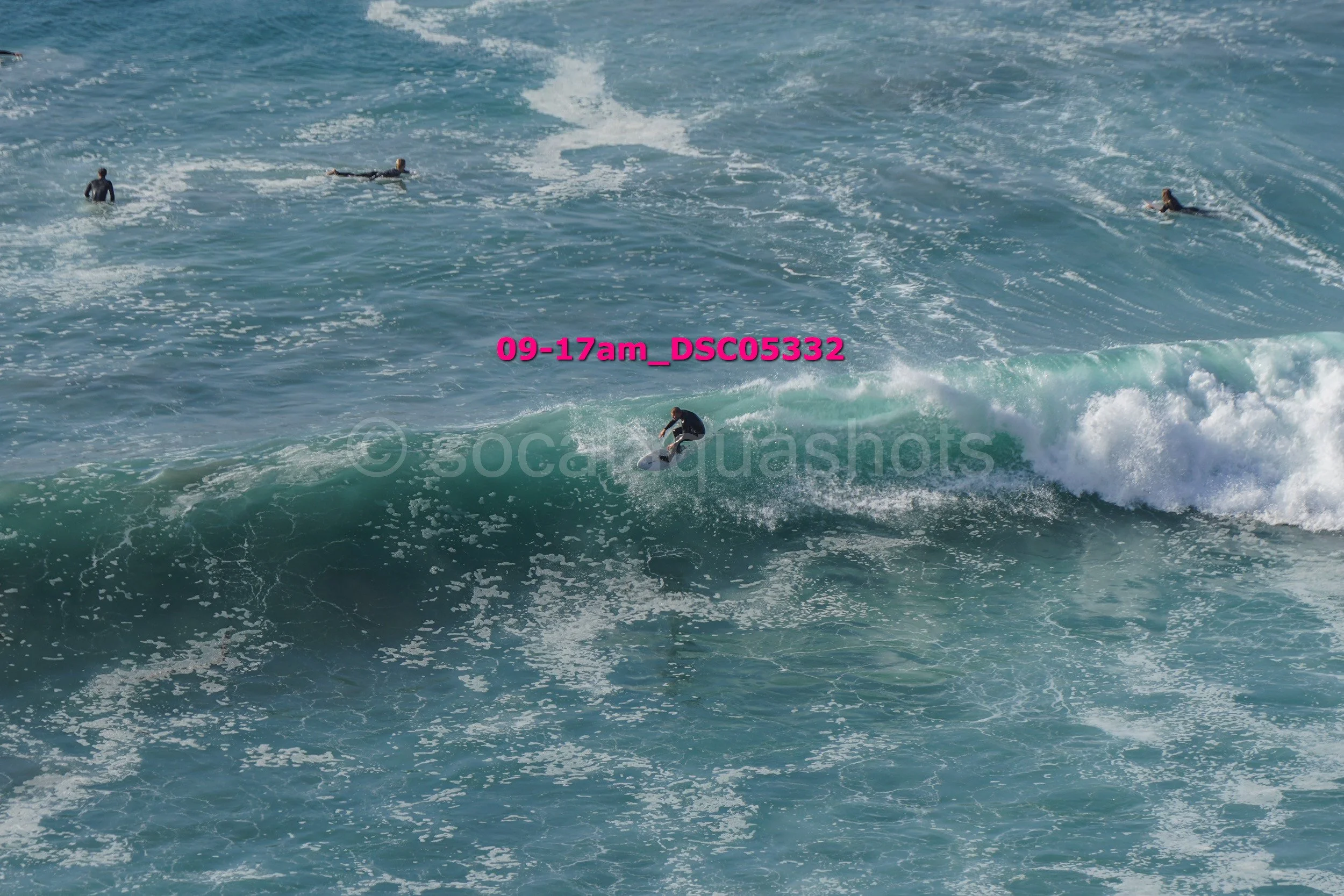 A person surfing on a wave with three other surfers in the water nearby.
