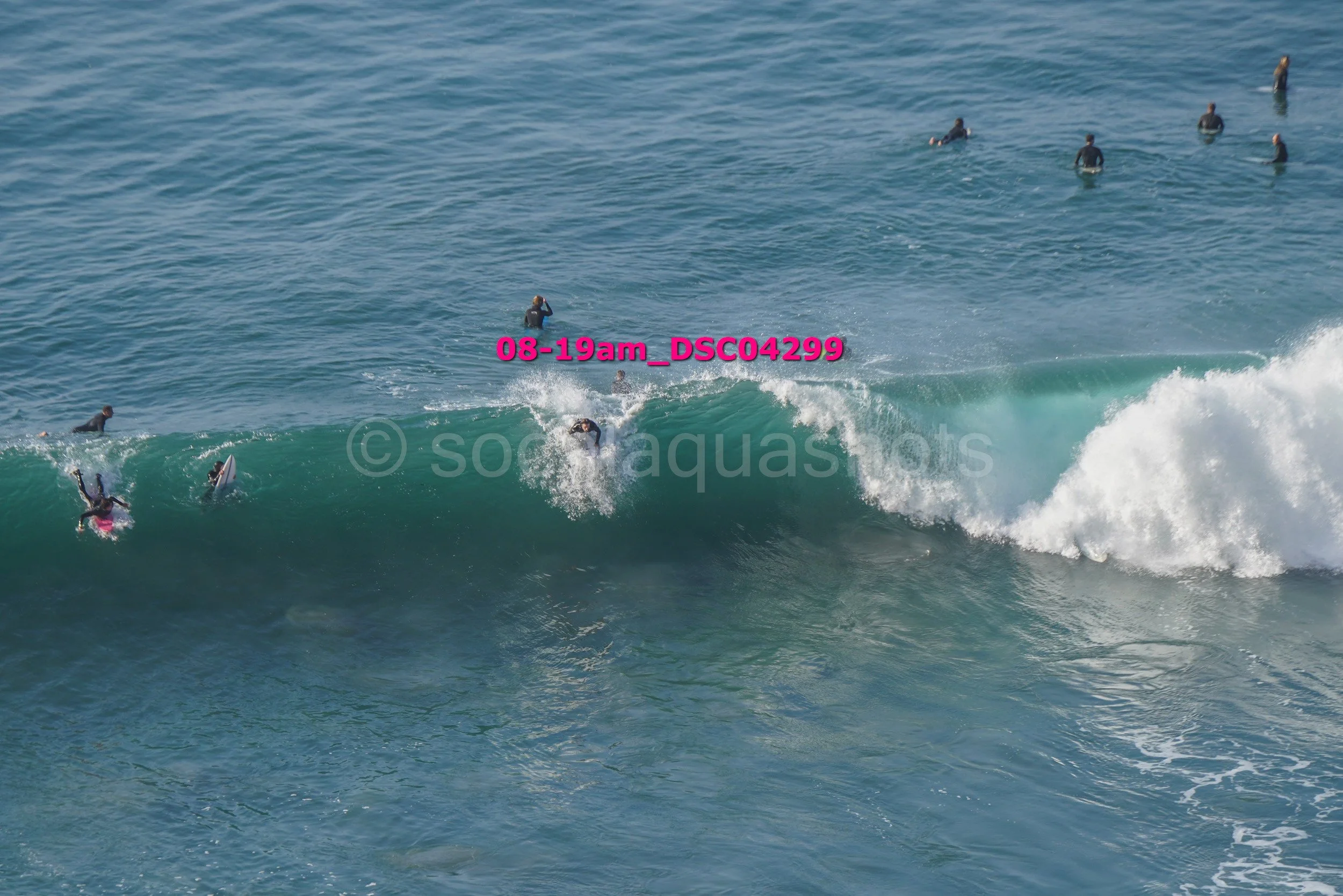 People surfing in the ocean, with some riding a wave and others waiting in the water.