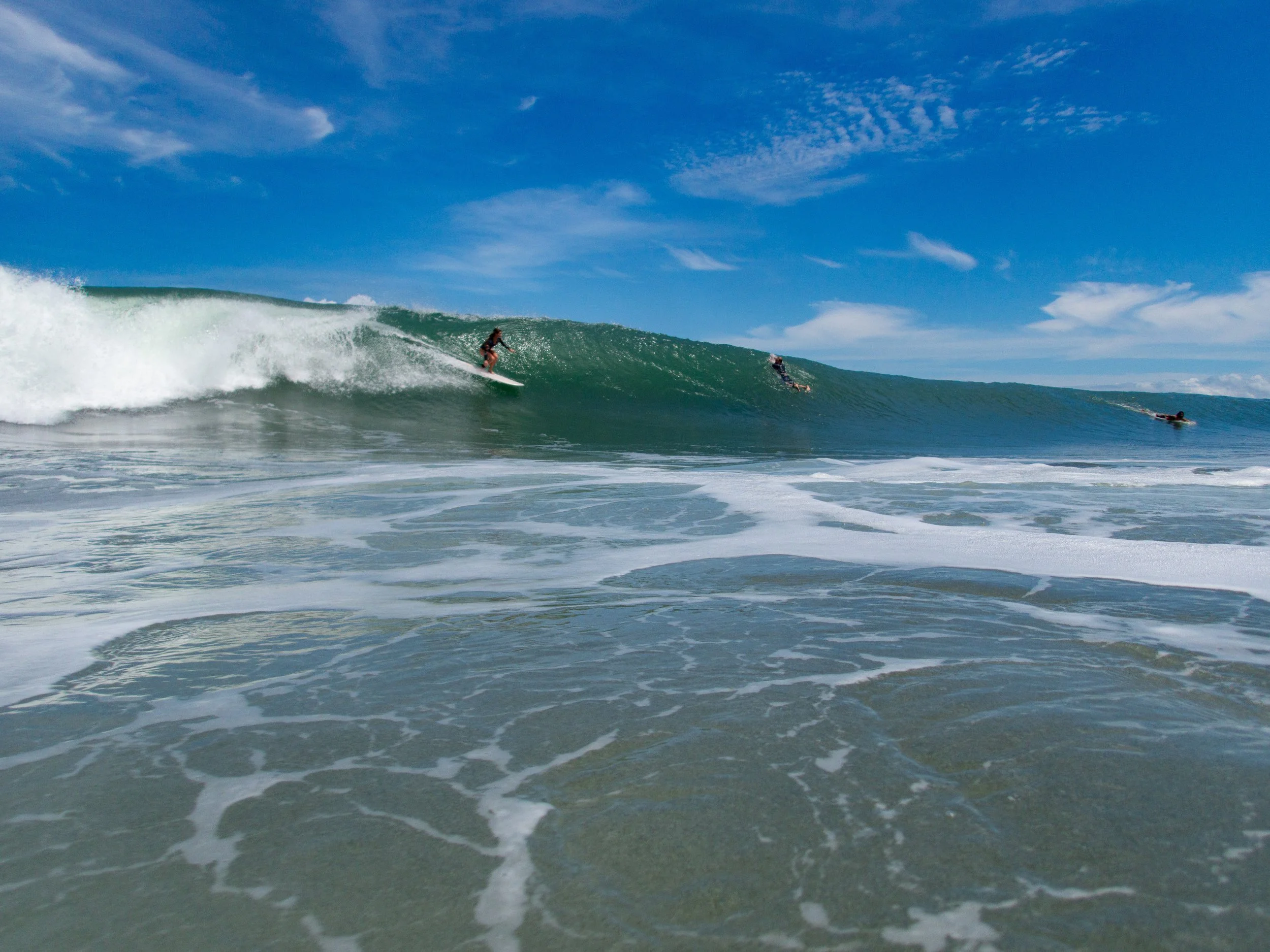 Surfers riding a wave on a beach with blue sky.