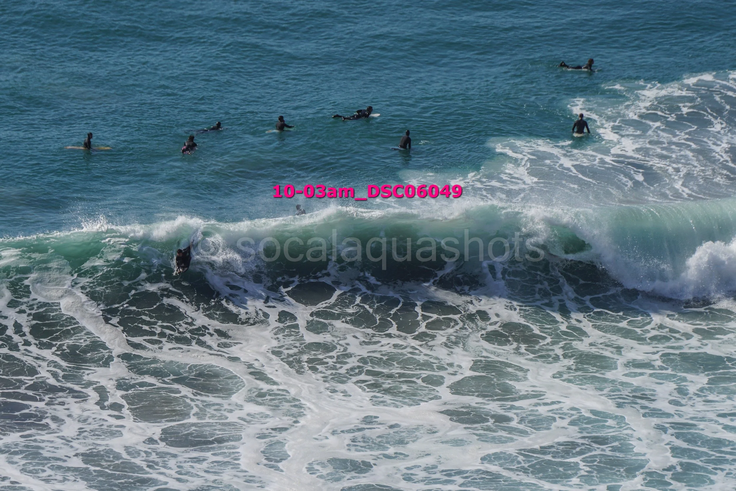 Group of surfers in the ocean, some riding waves and others swimming or paddling in the water.