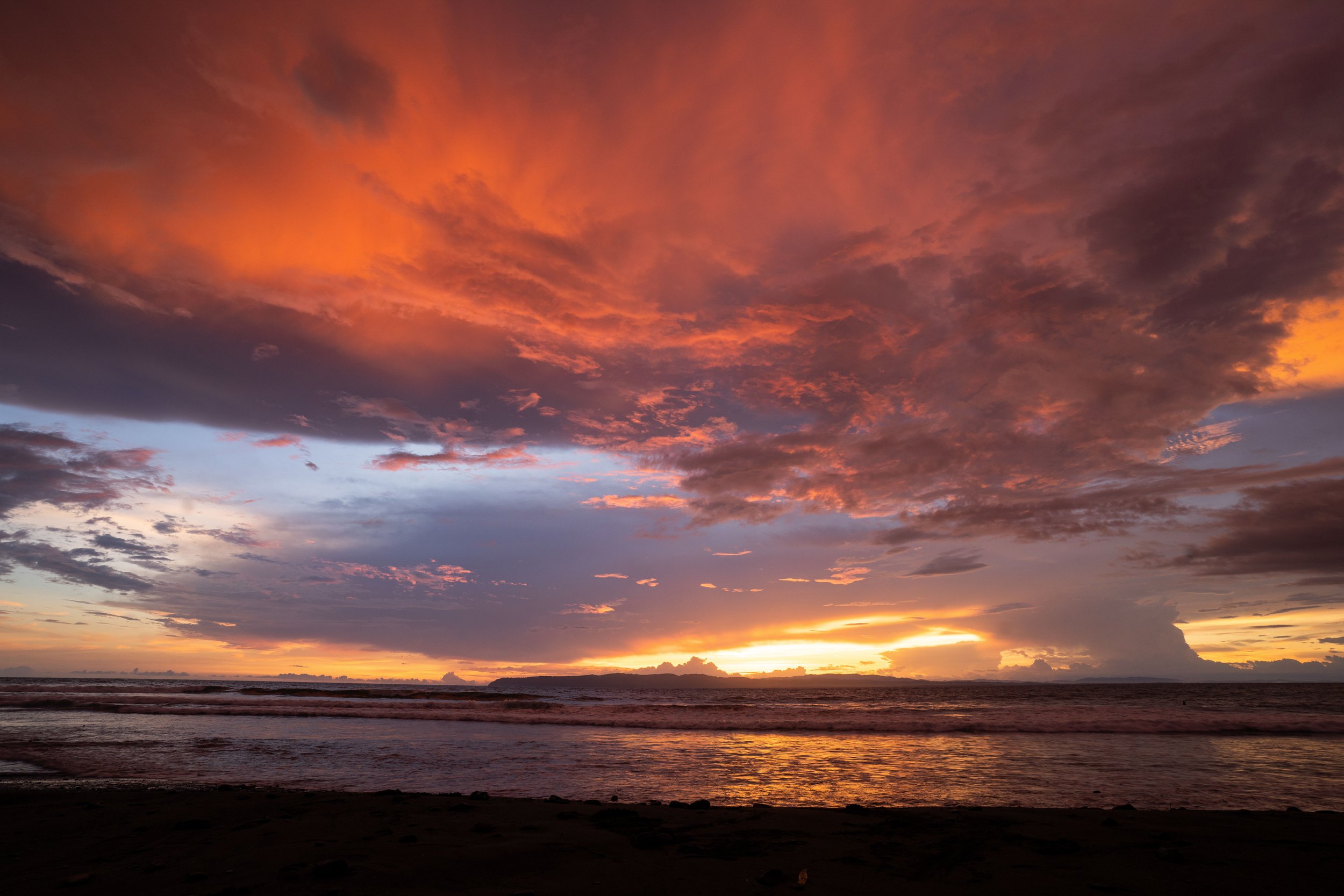 Sunset over the ocean with dark clouds and vibrant orange and purple hues in the sky.