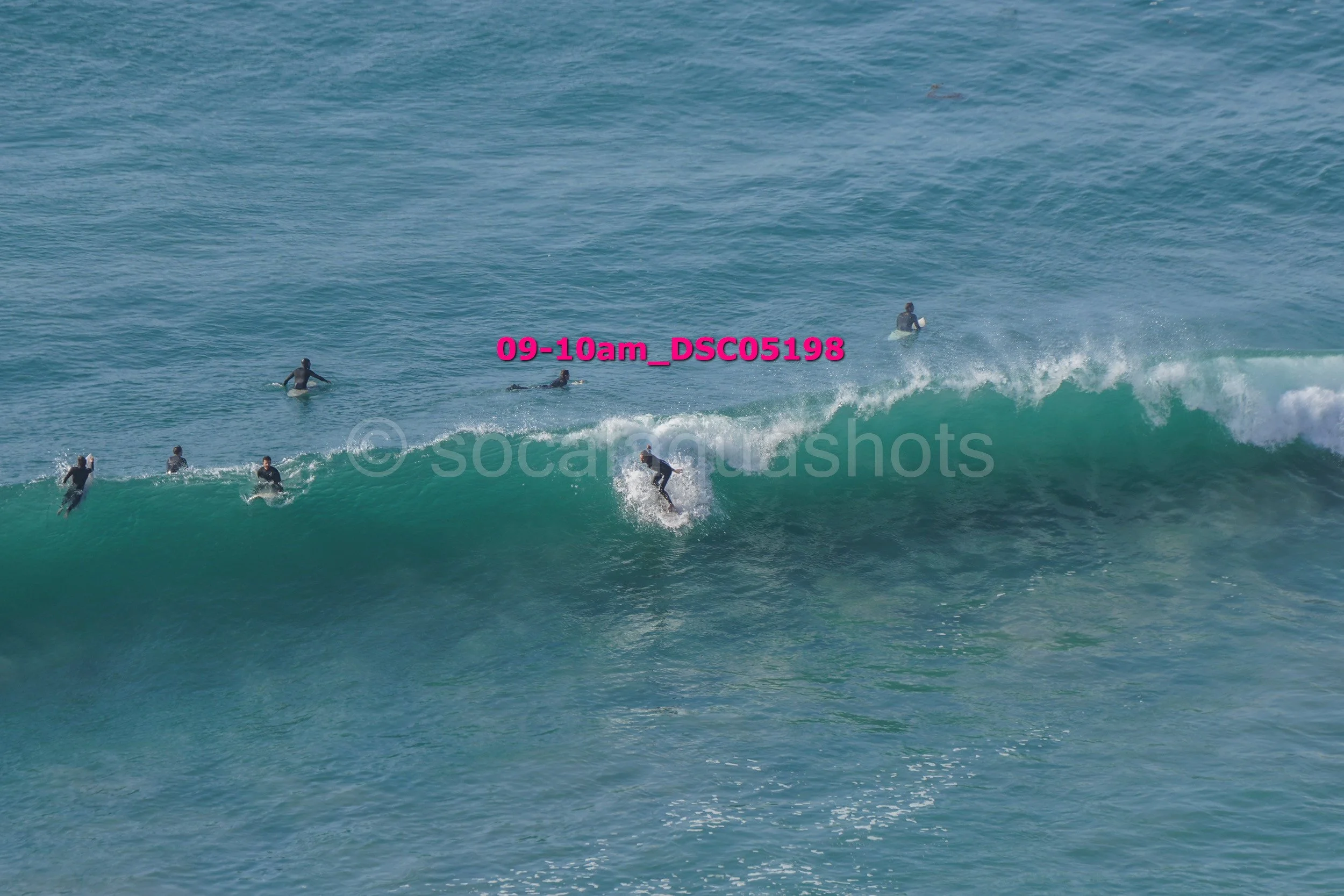 Surfers riding a large ocean wave with some surfers waiting in the water