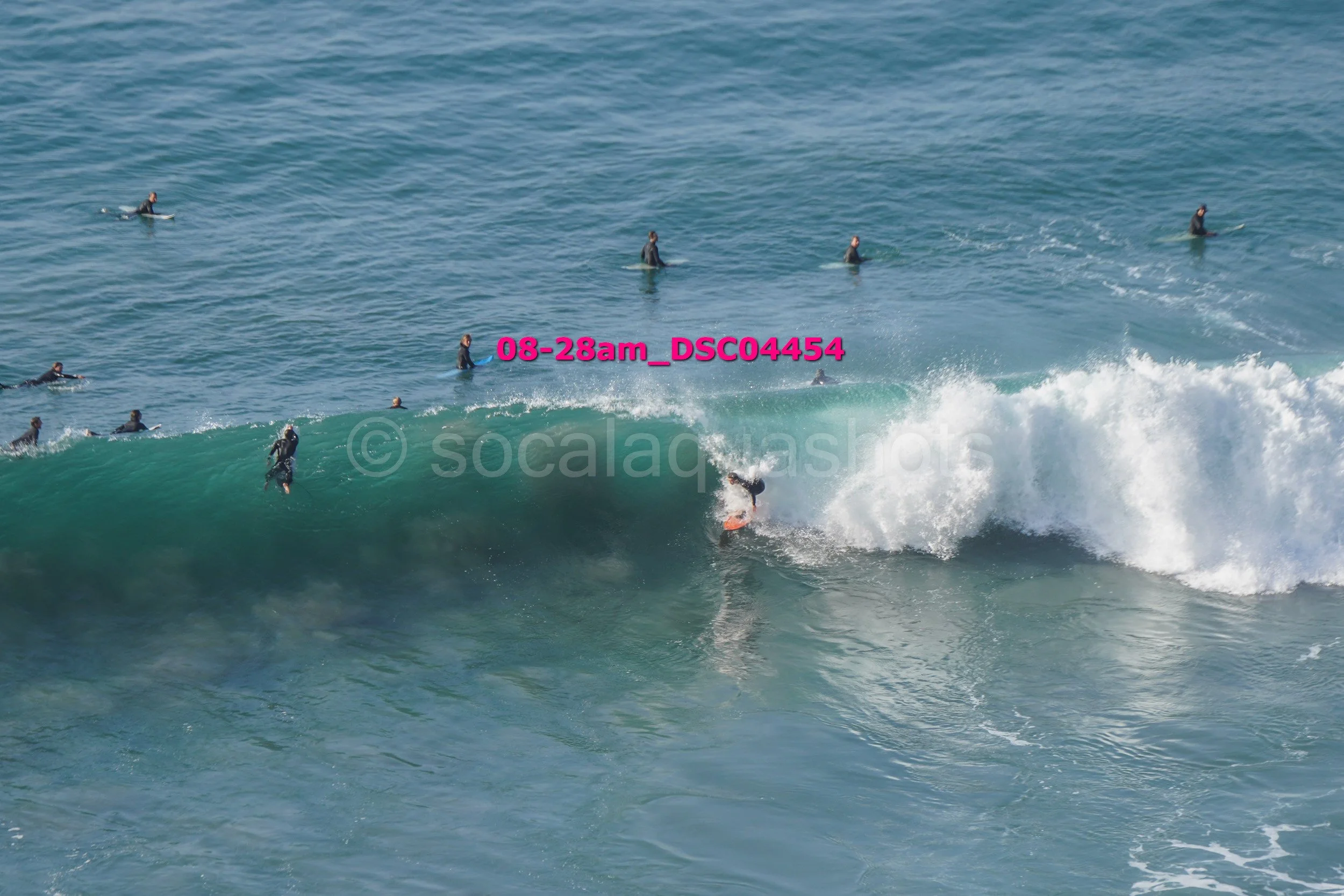 A group of people in wetsuits surfing on the ocean, with one surfer riding a wave while others wait in the water.