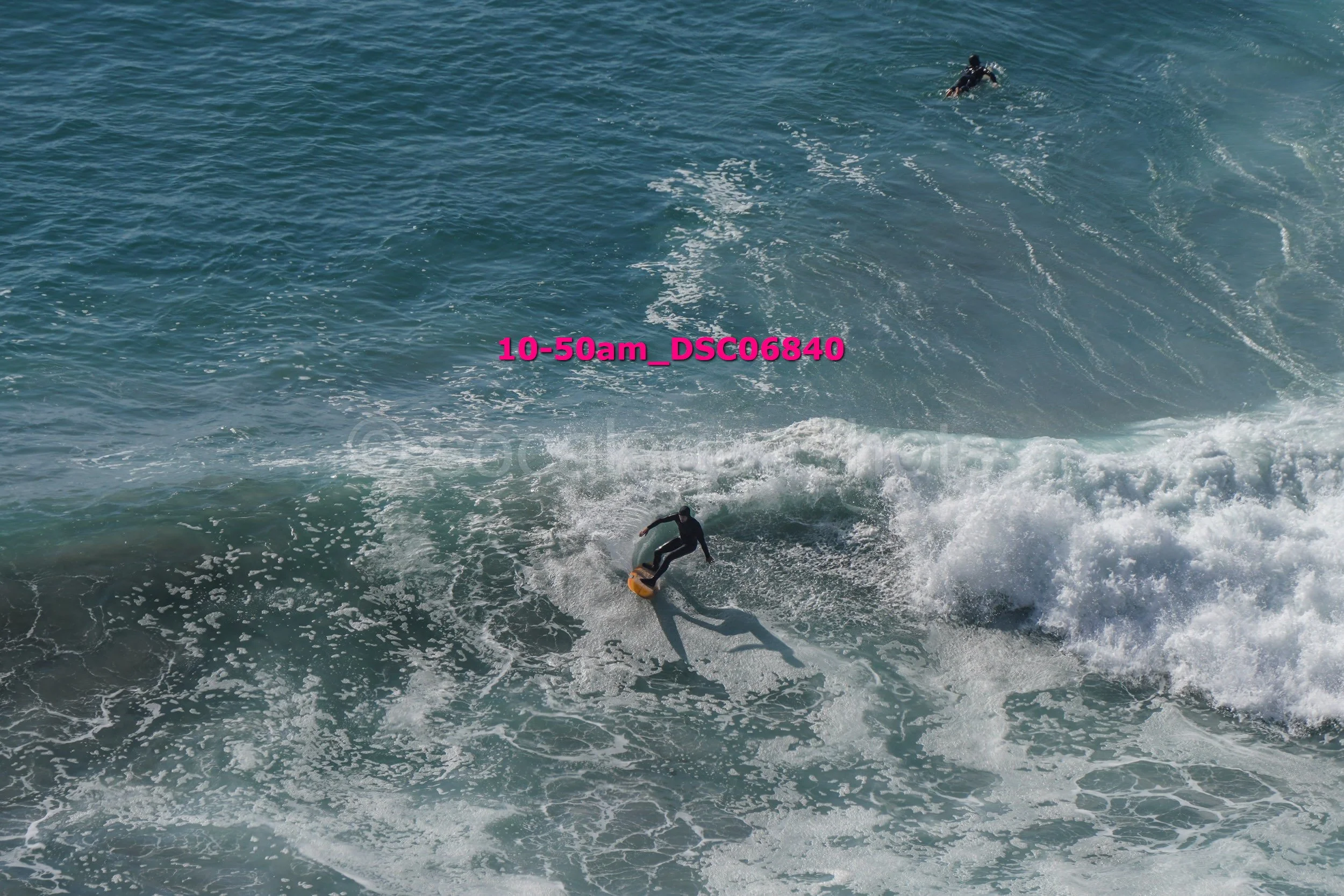 A person surfing on a wave in the ocean with another surfer in the water nearby.
