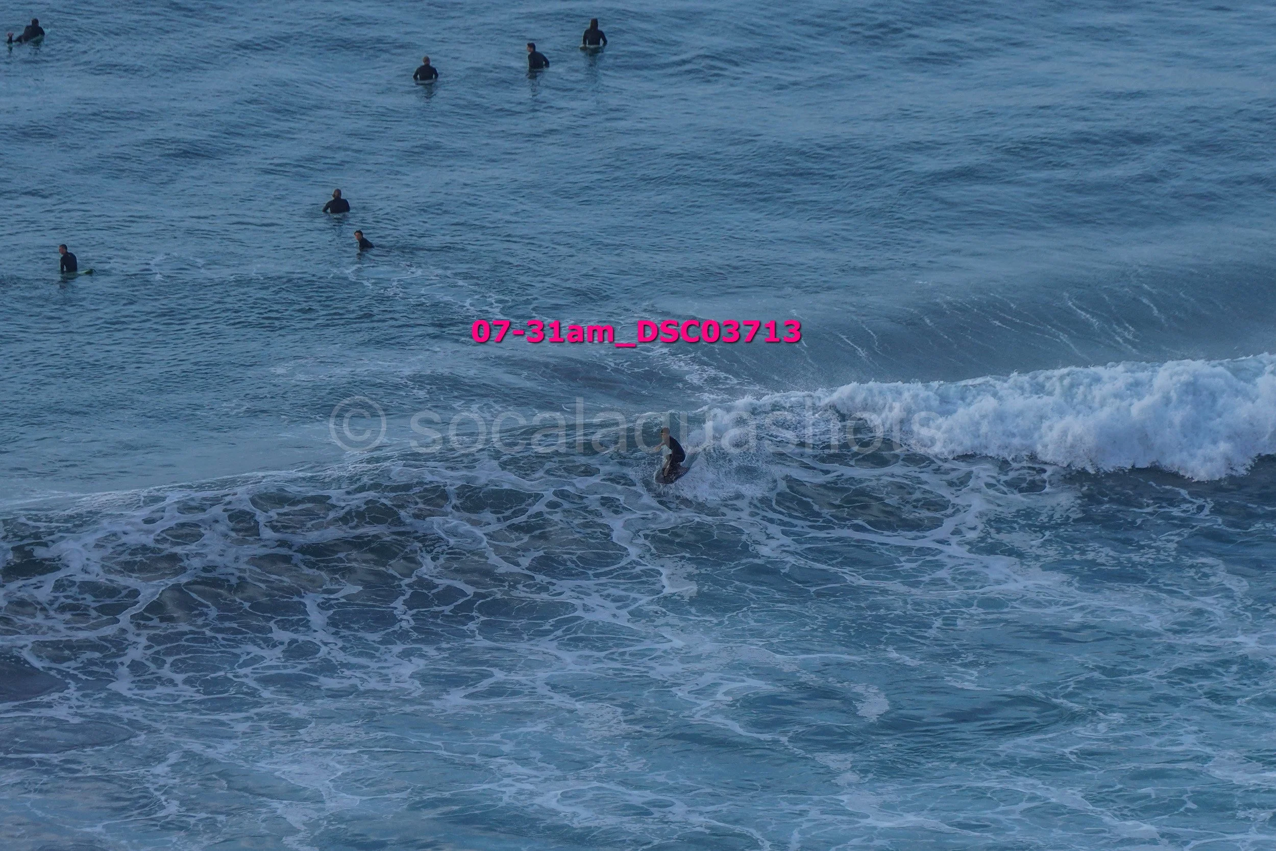 Multiple surfers waiting in the ocean, with one surfer riding a wave near the shore.