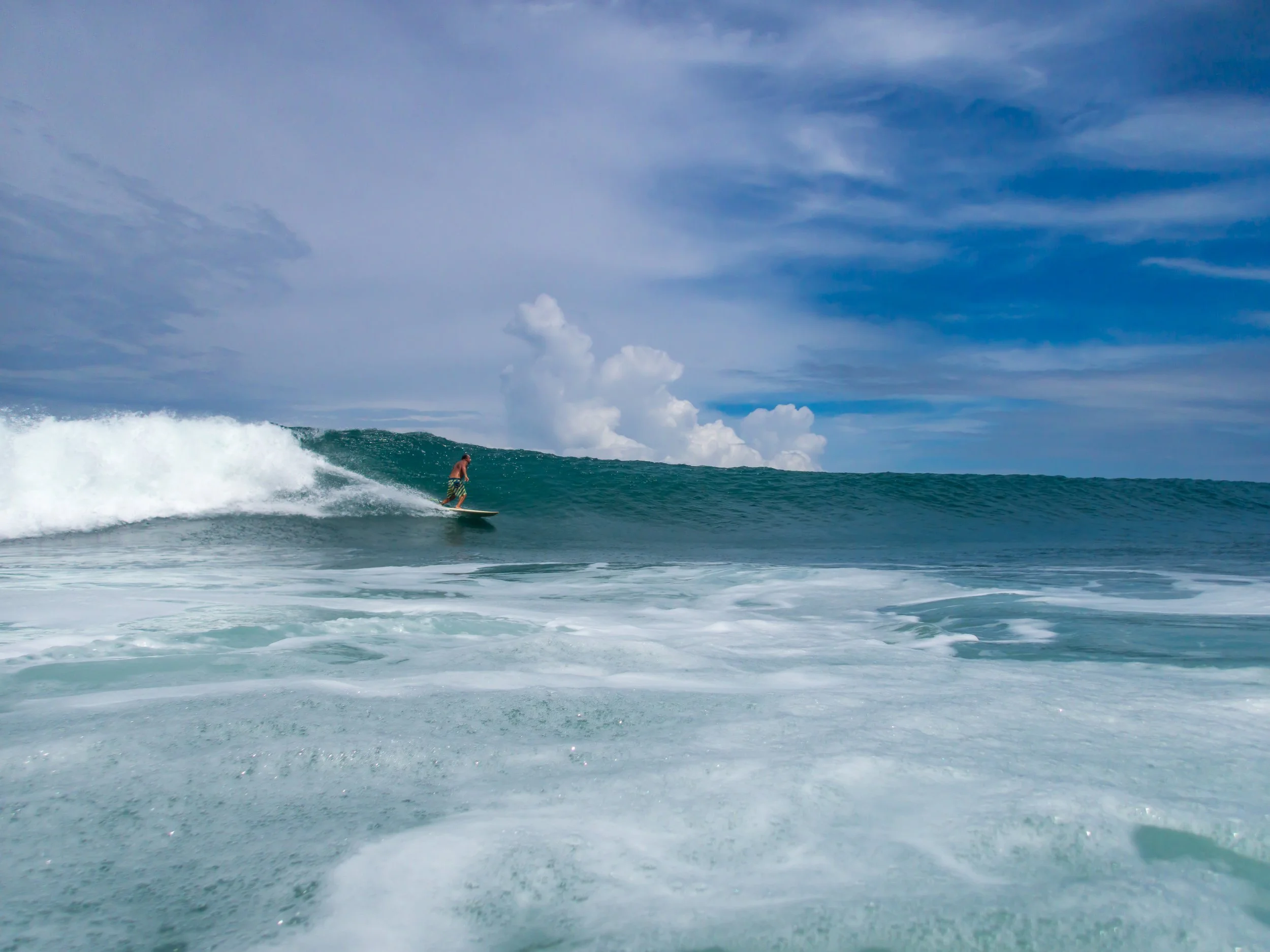 Surfer riding a wave under a blue sky with scattered clouds
