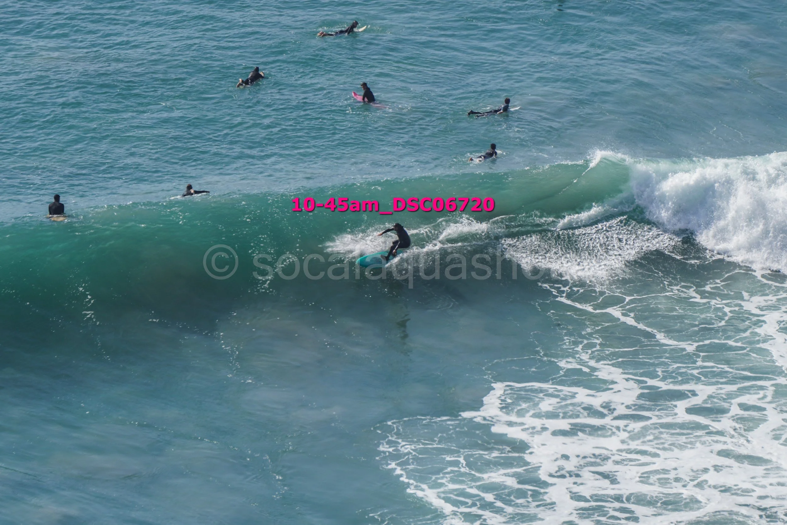 Surfer riding a wave with several people swimming and surfing in the water nearby.