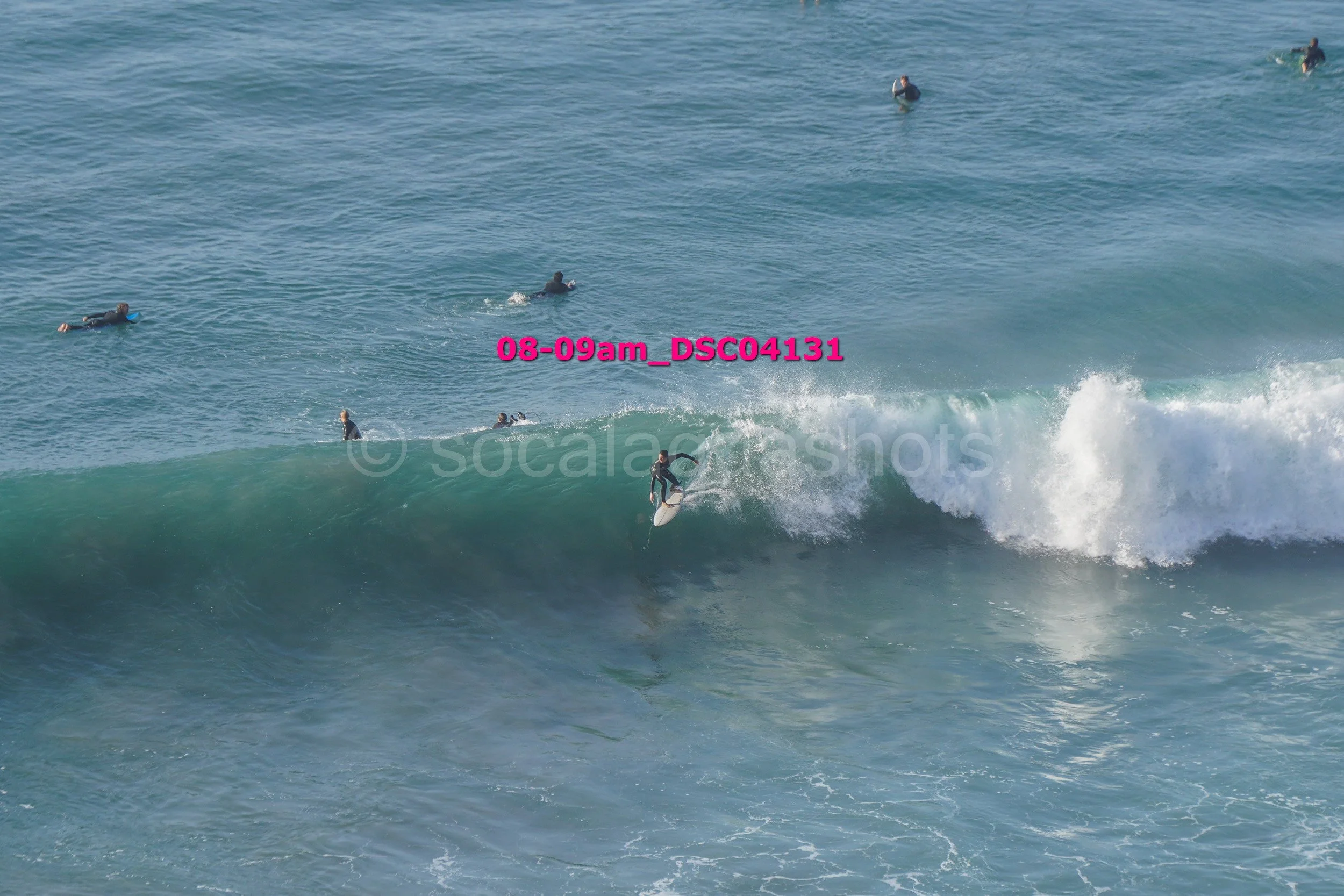 Surfer riding a wave with several other surfers waiting in the water nearby at the beach.
