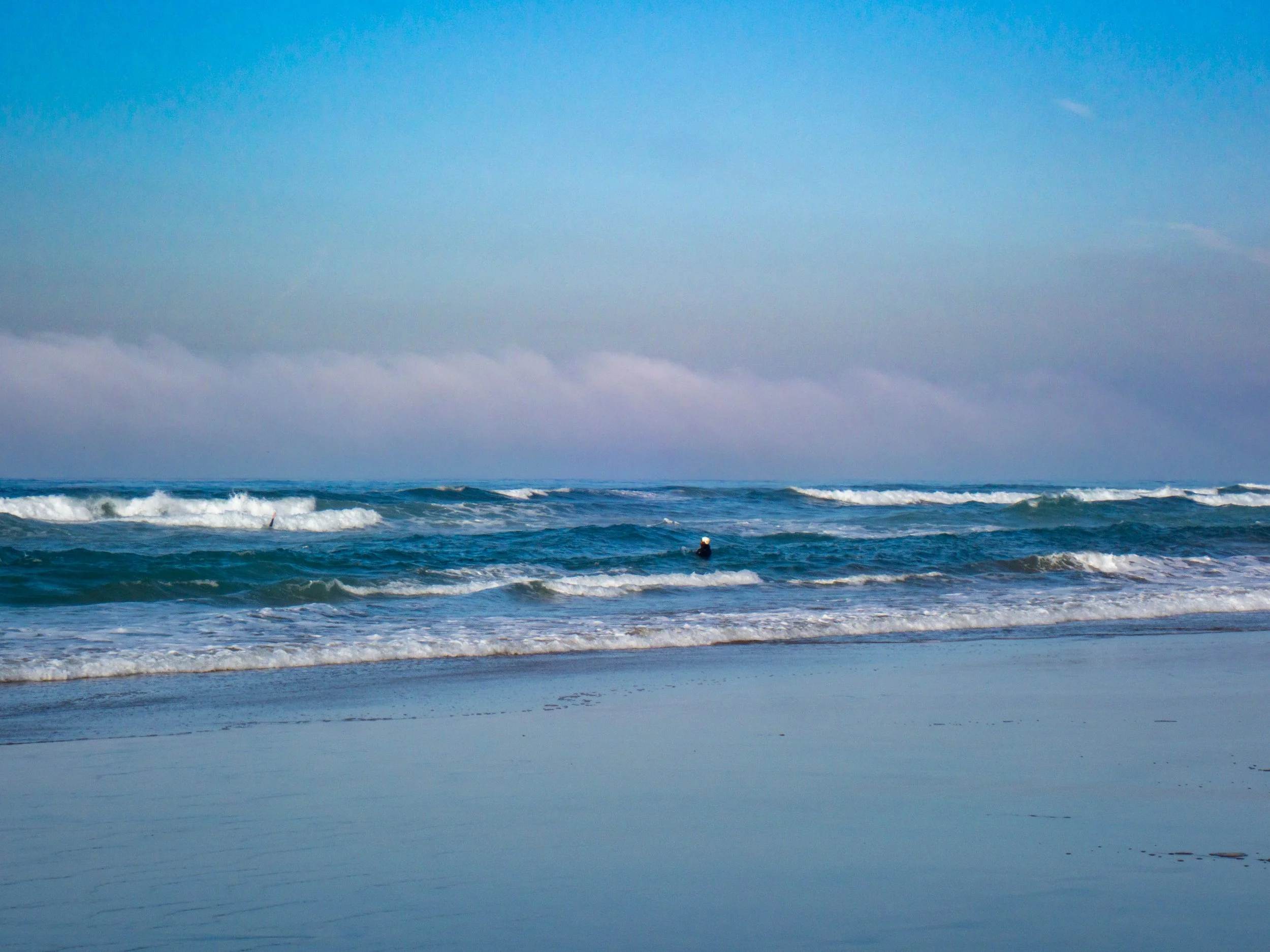 Ocean waves on a sandy beach with a person in the water, overcast sky.