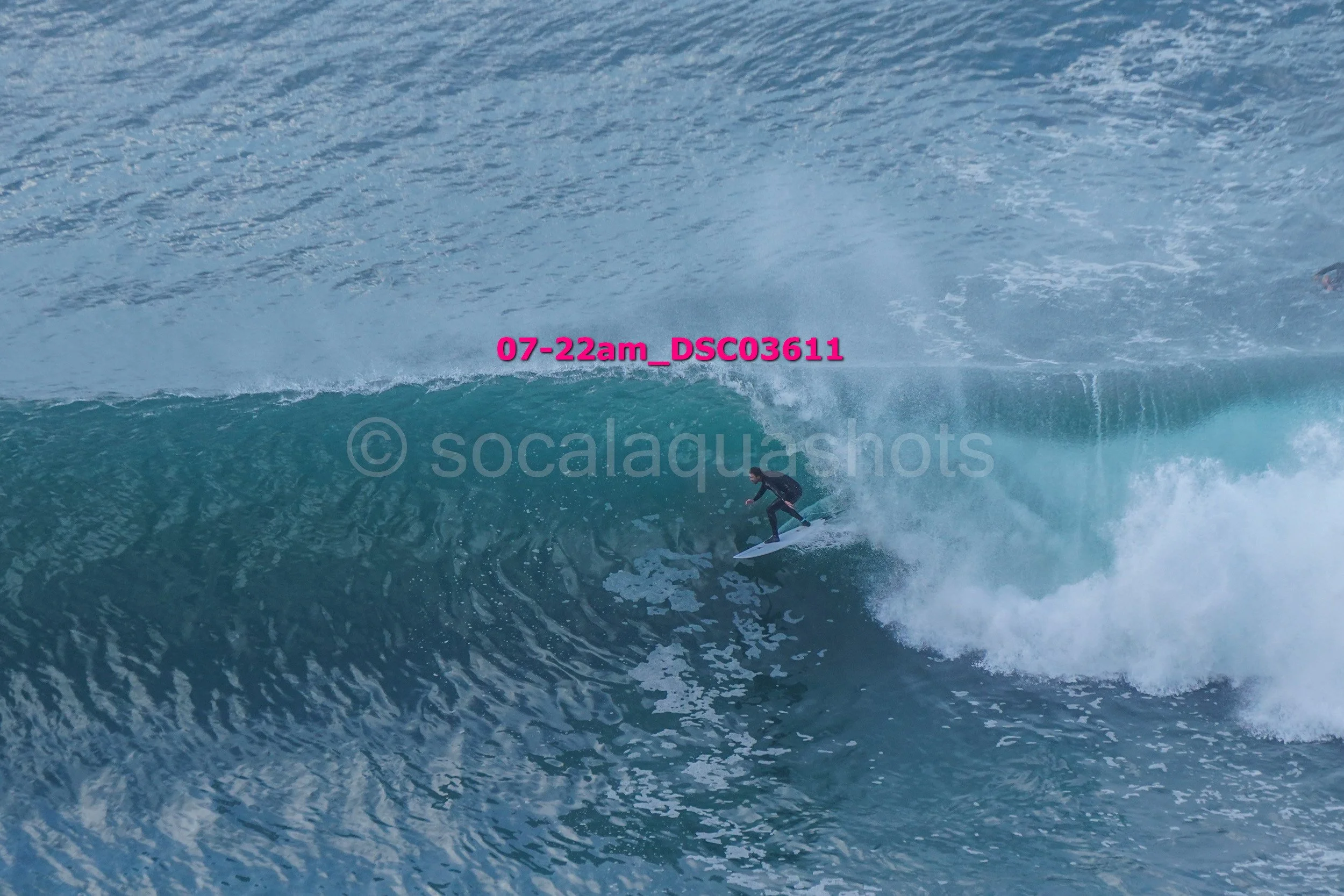 A person in black wetsuit surfing a large blue wave in the ocean.