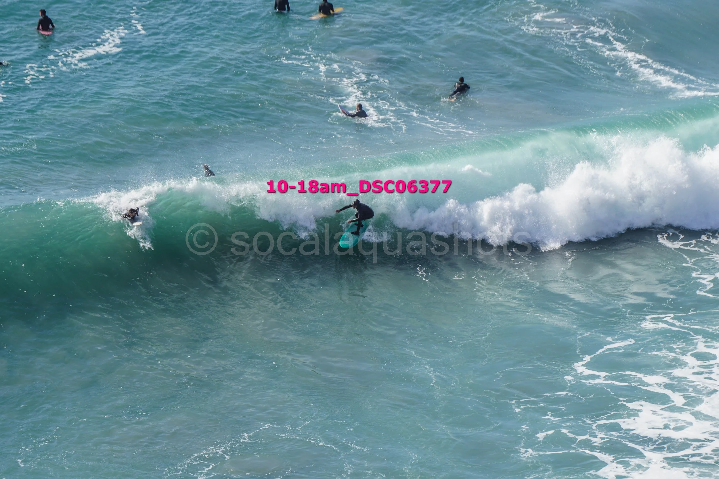 A person surfing on a large wave while other surfers and swimmers are in the water nearby.