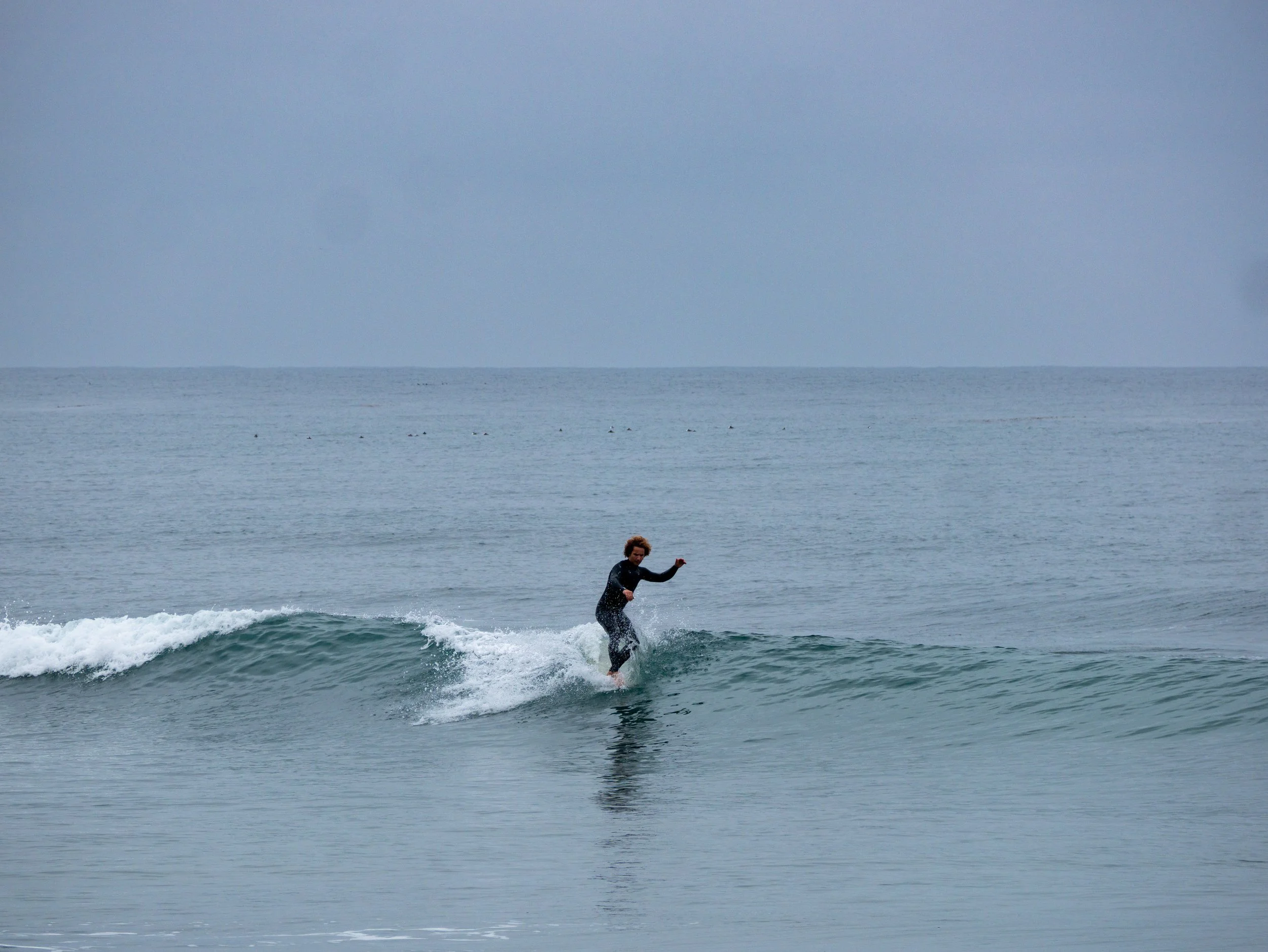 A person surfing on a small wave in the ocean on a cloudy day.