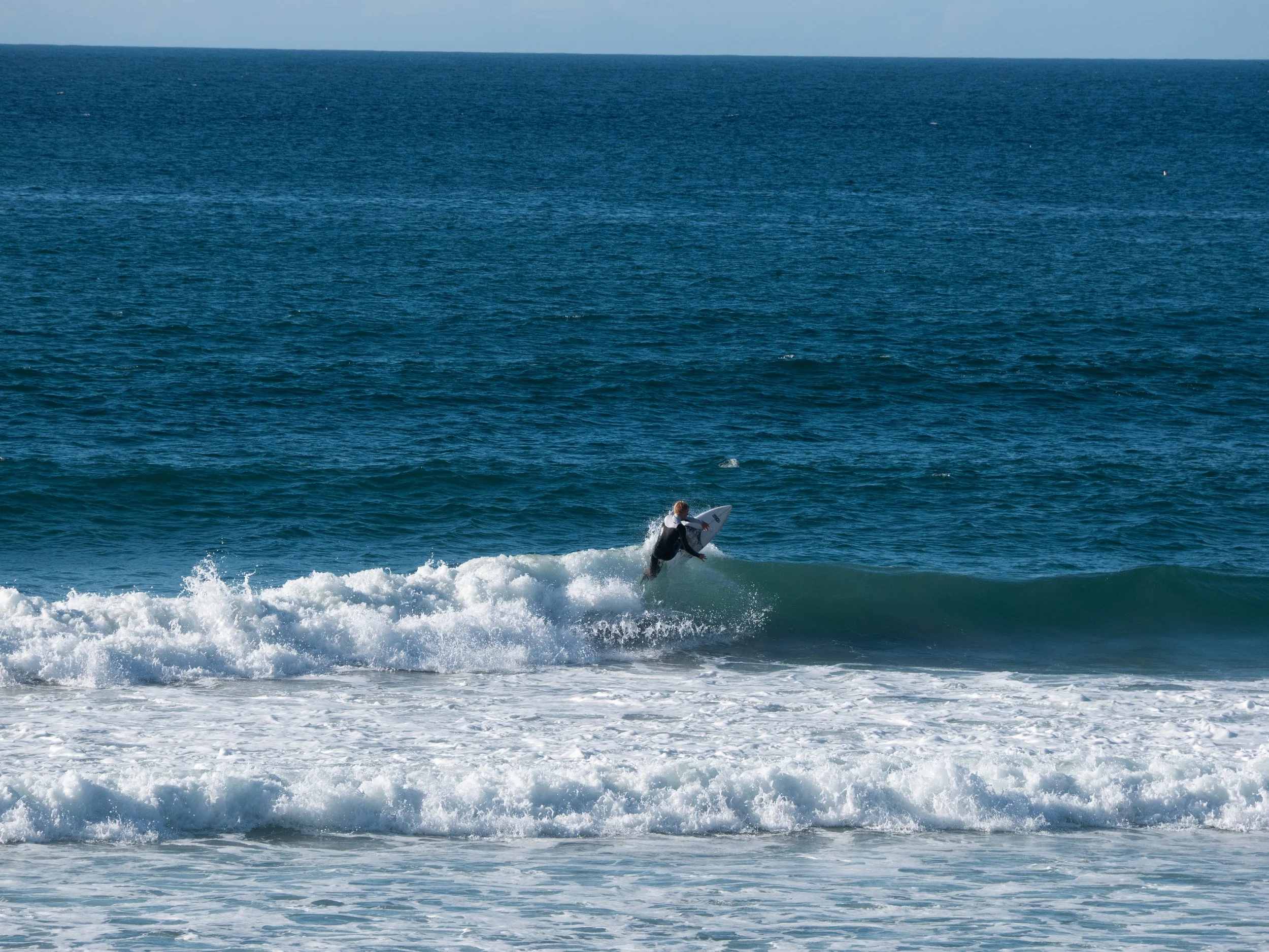 Surfer riding a wave in the ocean with clear blue water and sky.