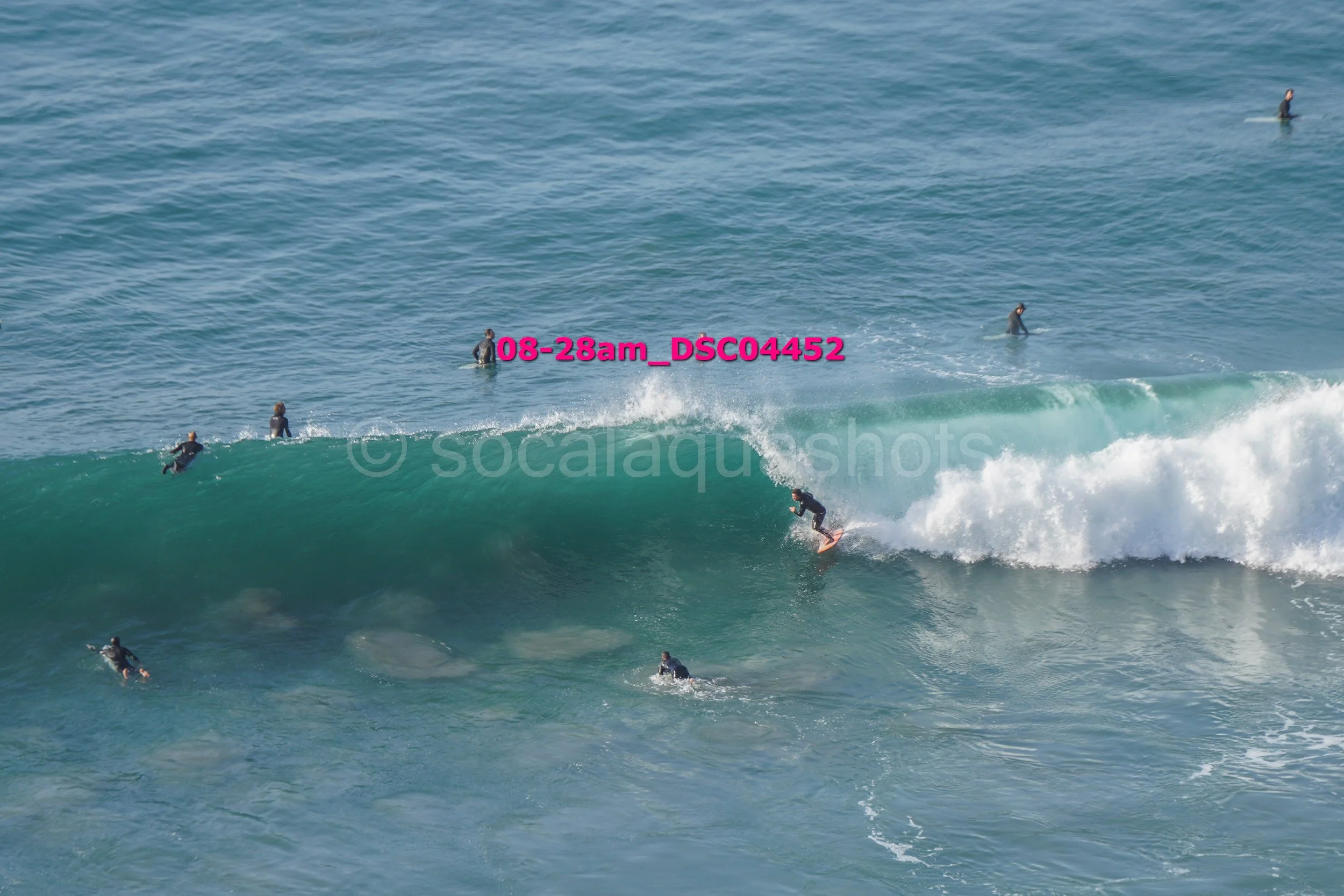 Surfer riding a wave with multiple surfers and paddleboarders in the background at the ocean.