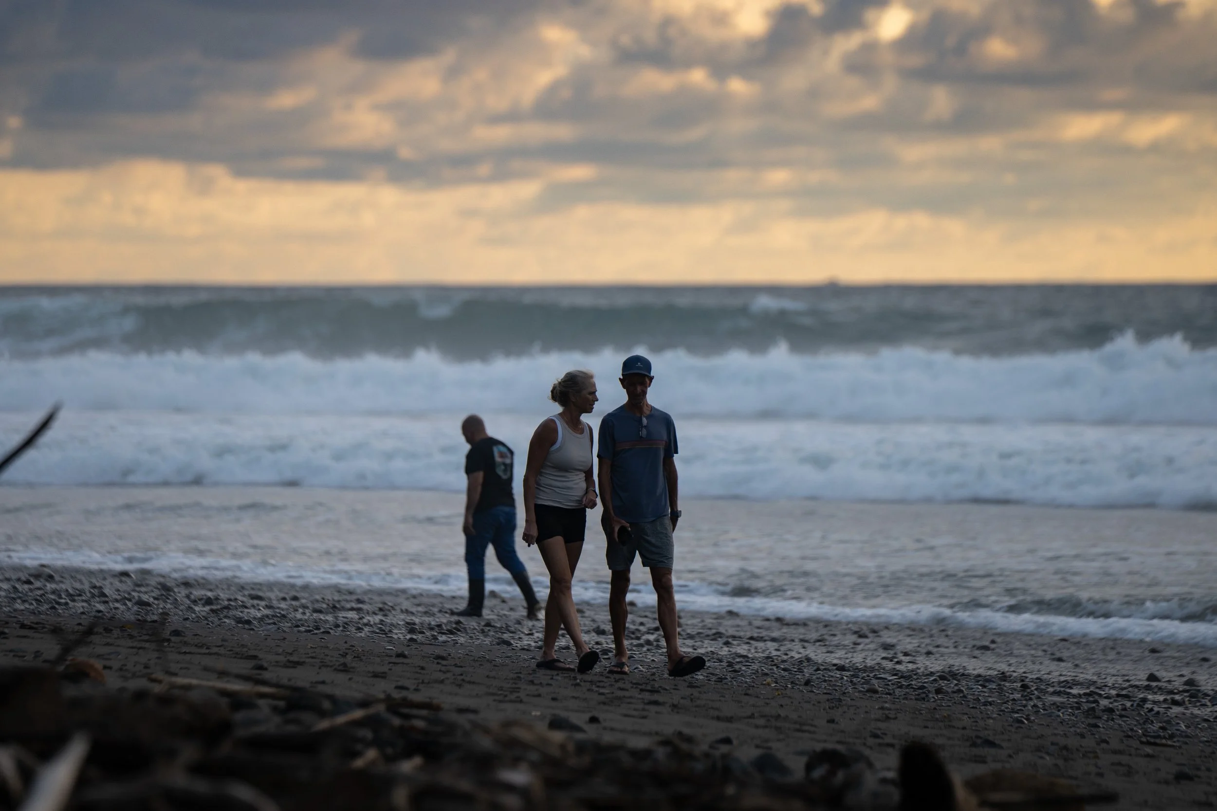 People walking on a beach near the ocean during sunset, with clouds in the sky.
