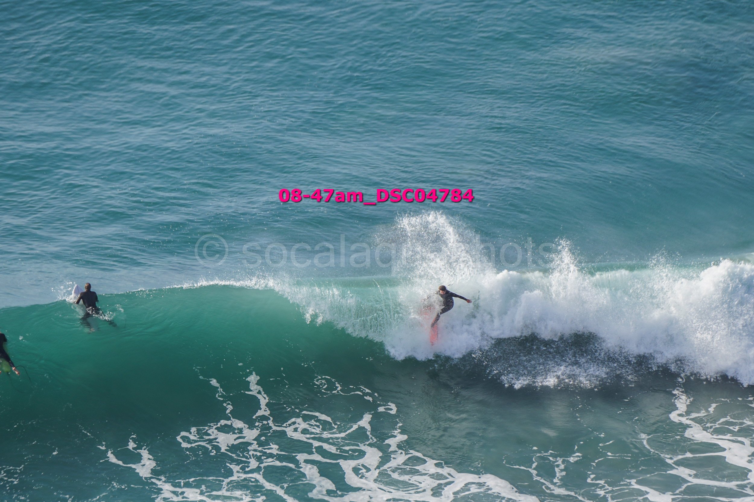 Three surfers riding and paddling on ocean waves in sunny weather.