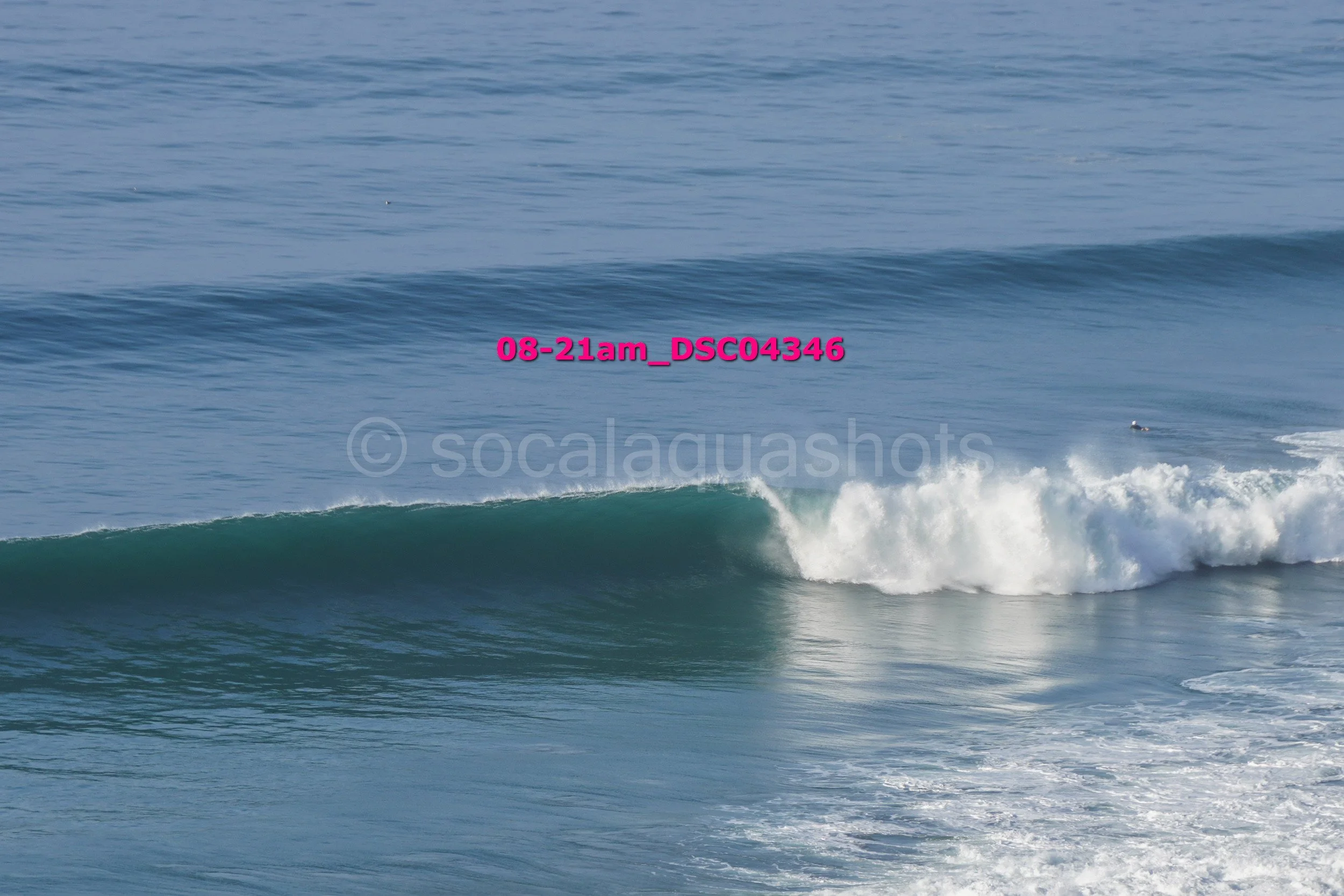 Ocean waves with one wave cresting and white foam, under clear sky.