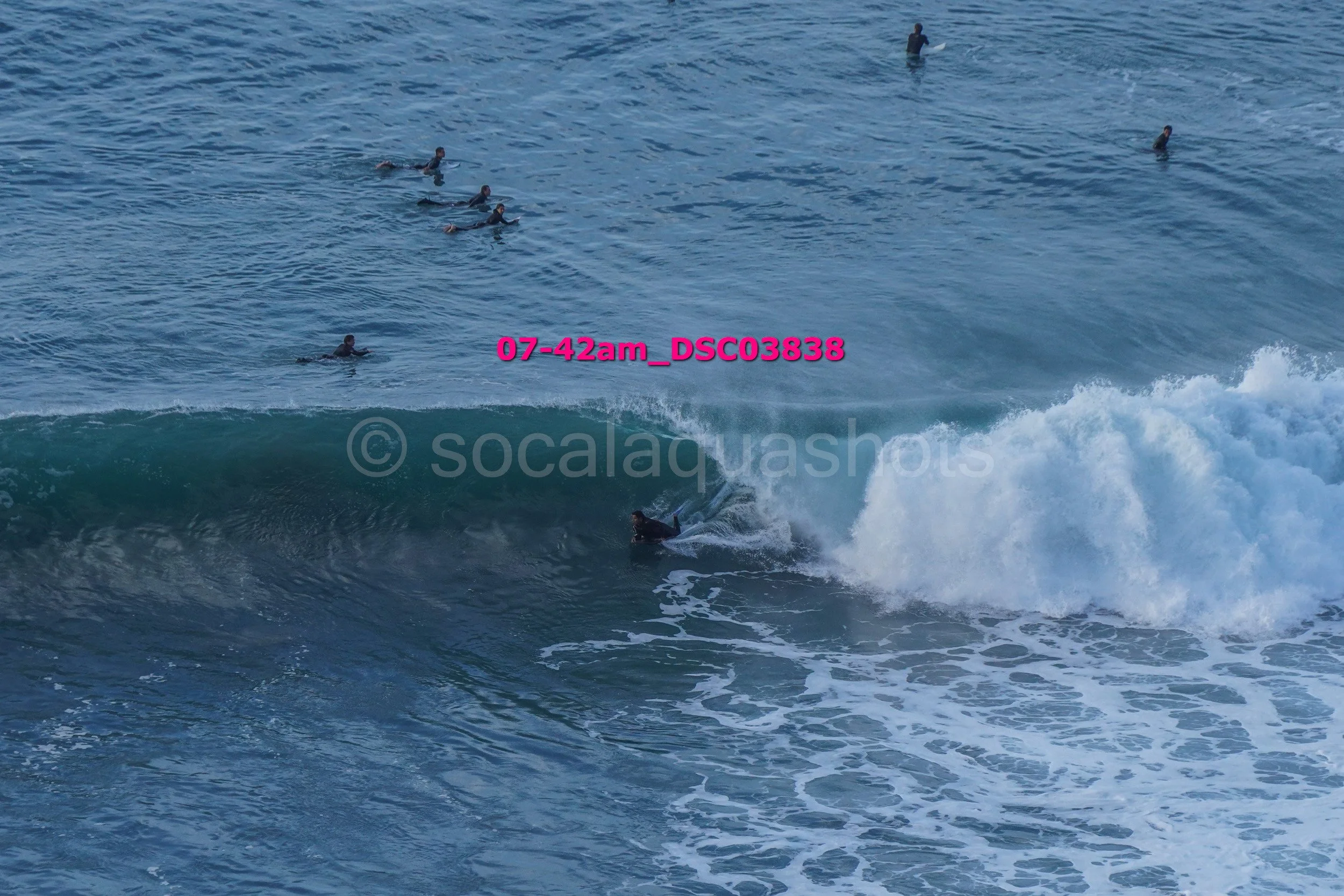 Surfer riding a wave with several people swimming and surfing in the background in the ocean.