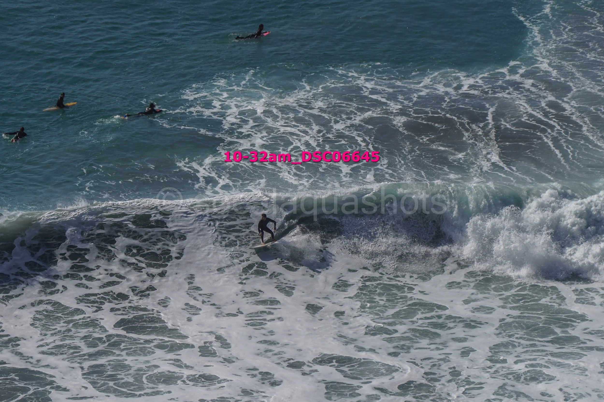 Surfer riding a wave with several surfers in the water nearby at the beach.