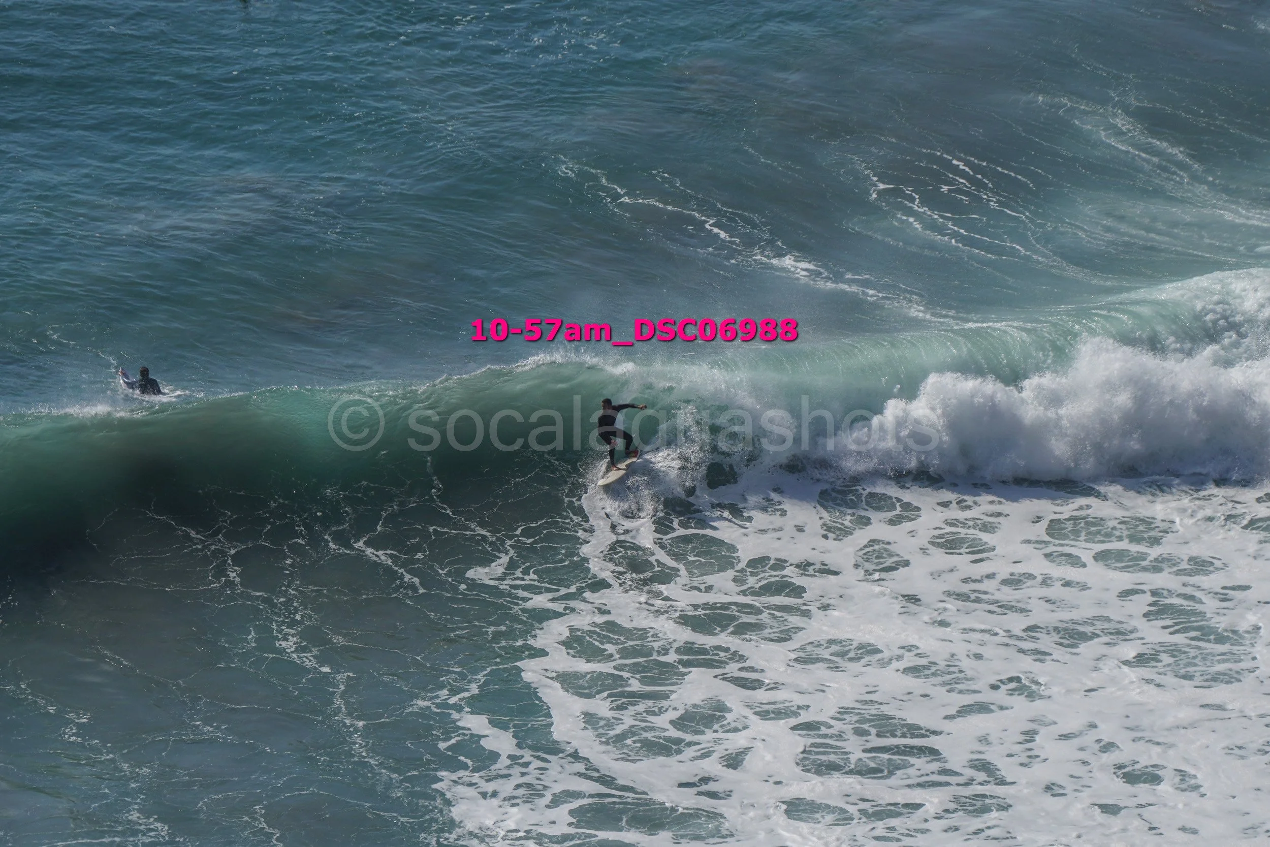 A person surfing on a wave in the ocean with another person swimming nearby.