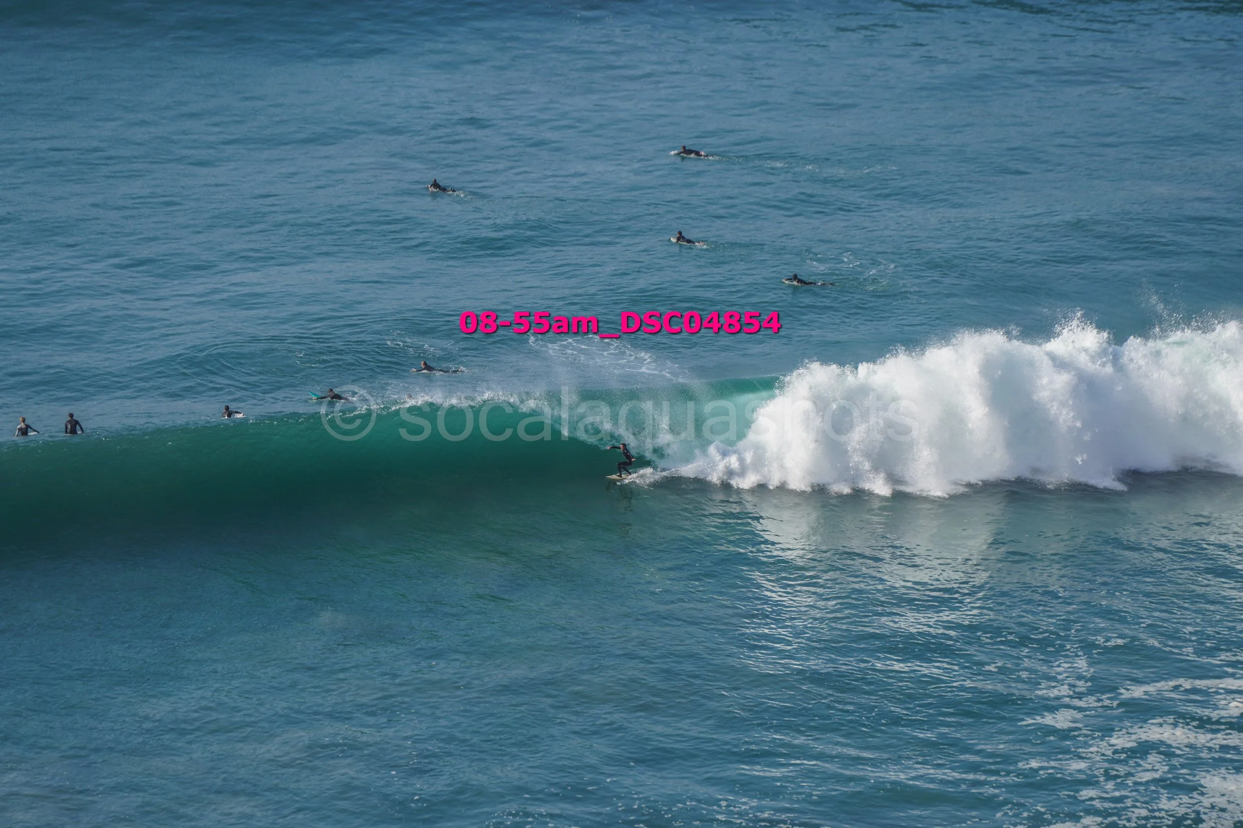 Surfer riding a large wave with several surfers in the background in the ocean.