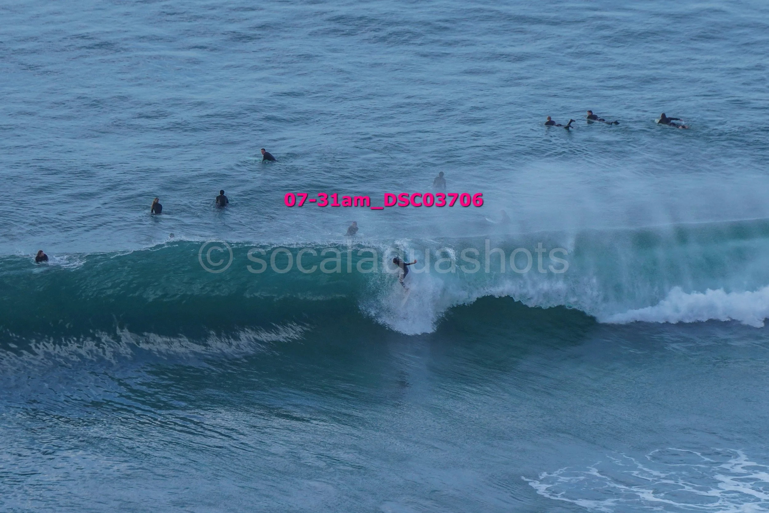 Surfer riding a wave with multiple surfers in the water in the background.