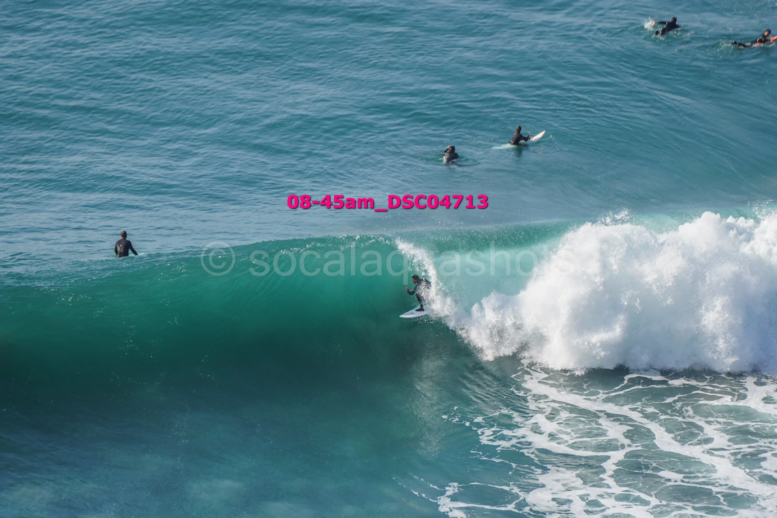 Surfer riding a large wave with several surfers in the background in the water.