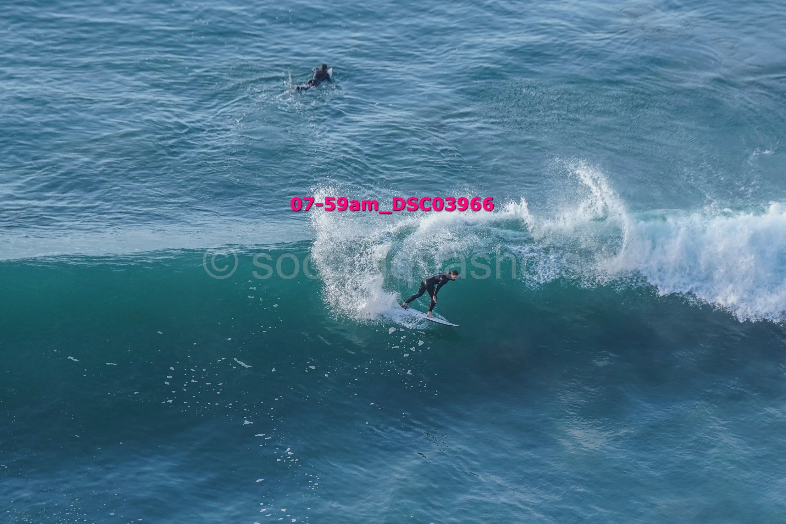 Surfer riding a large wave with another person in the background in the ocean.