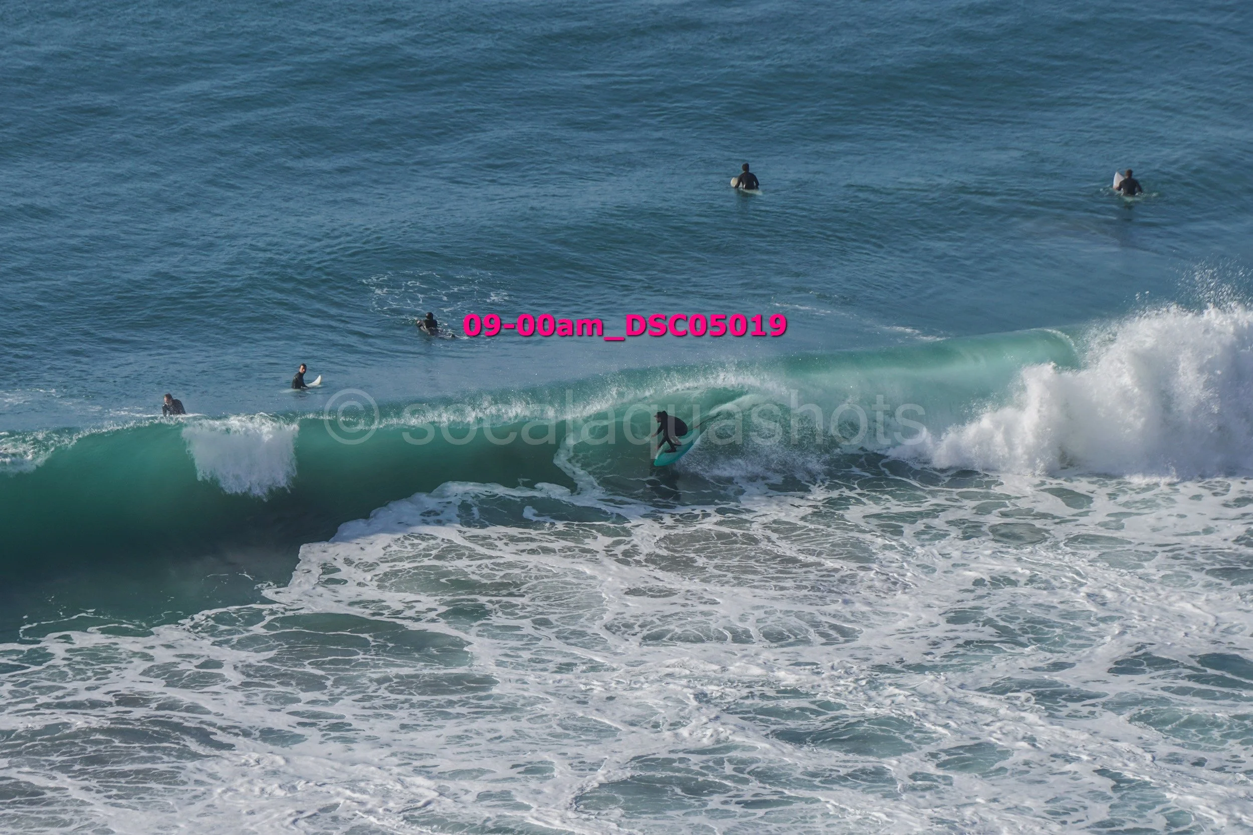 A surfer riding a wave while several surfers wait in the water.