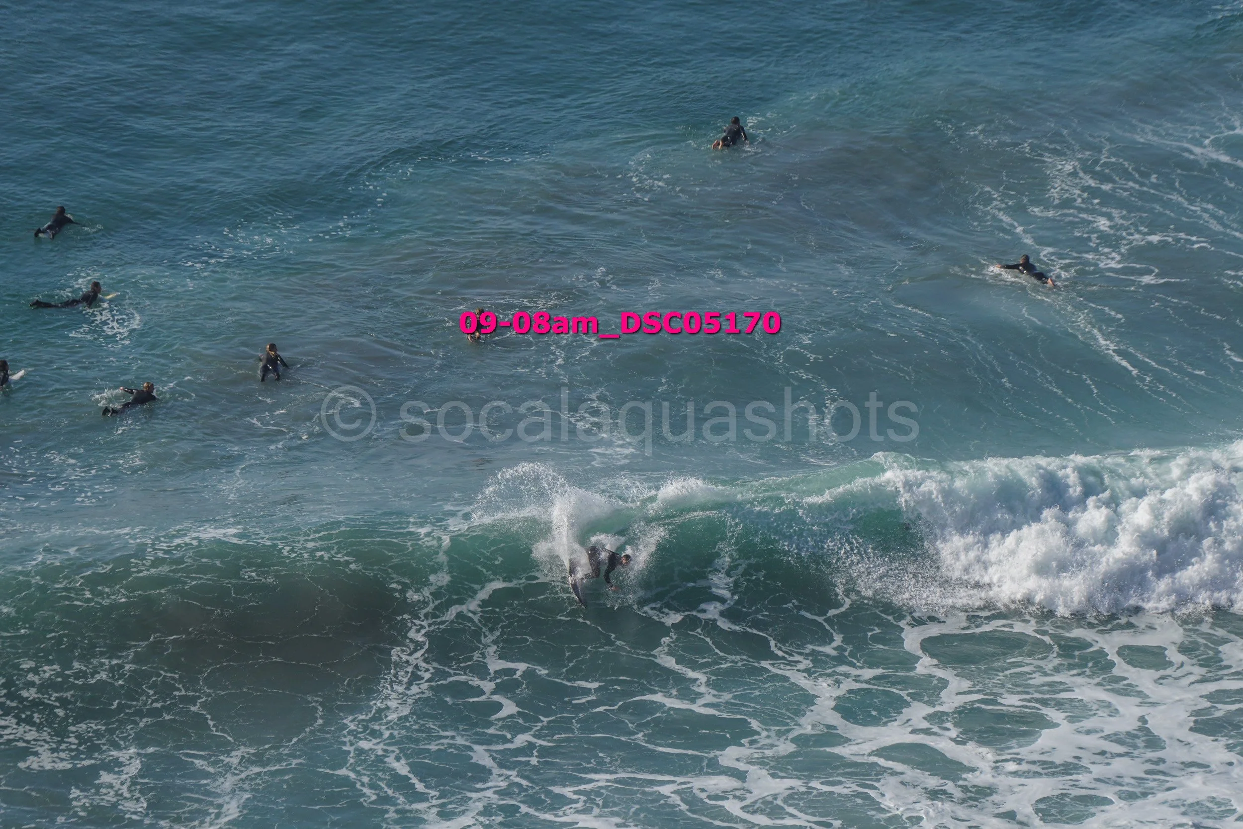 A group of people surfing in the ocean with one person riding a wave in the foreground.