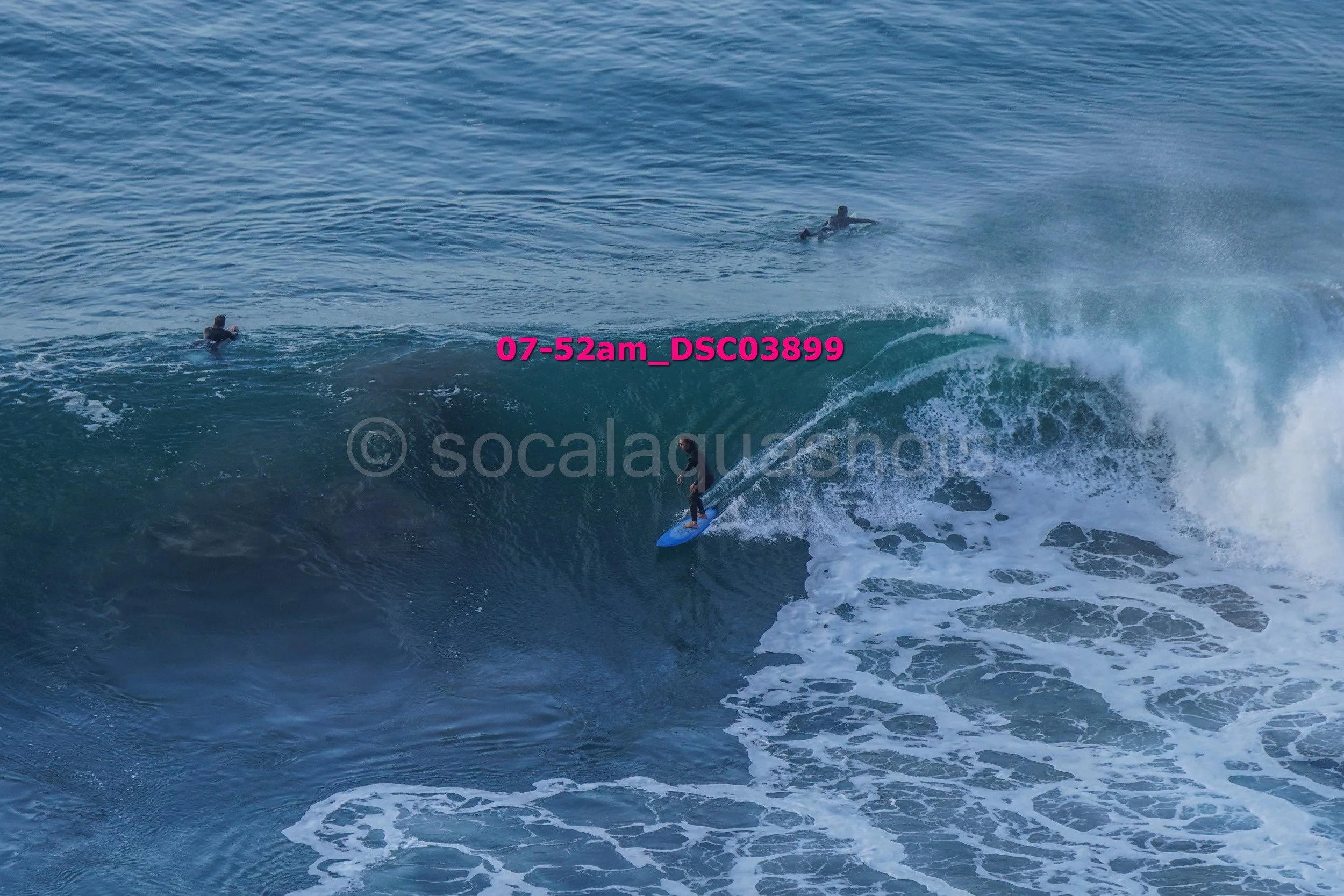 A surfer riding a large wave with two other surfers nearby in the water.