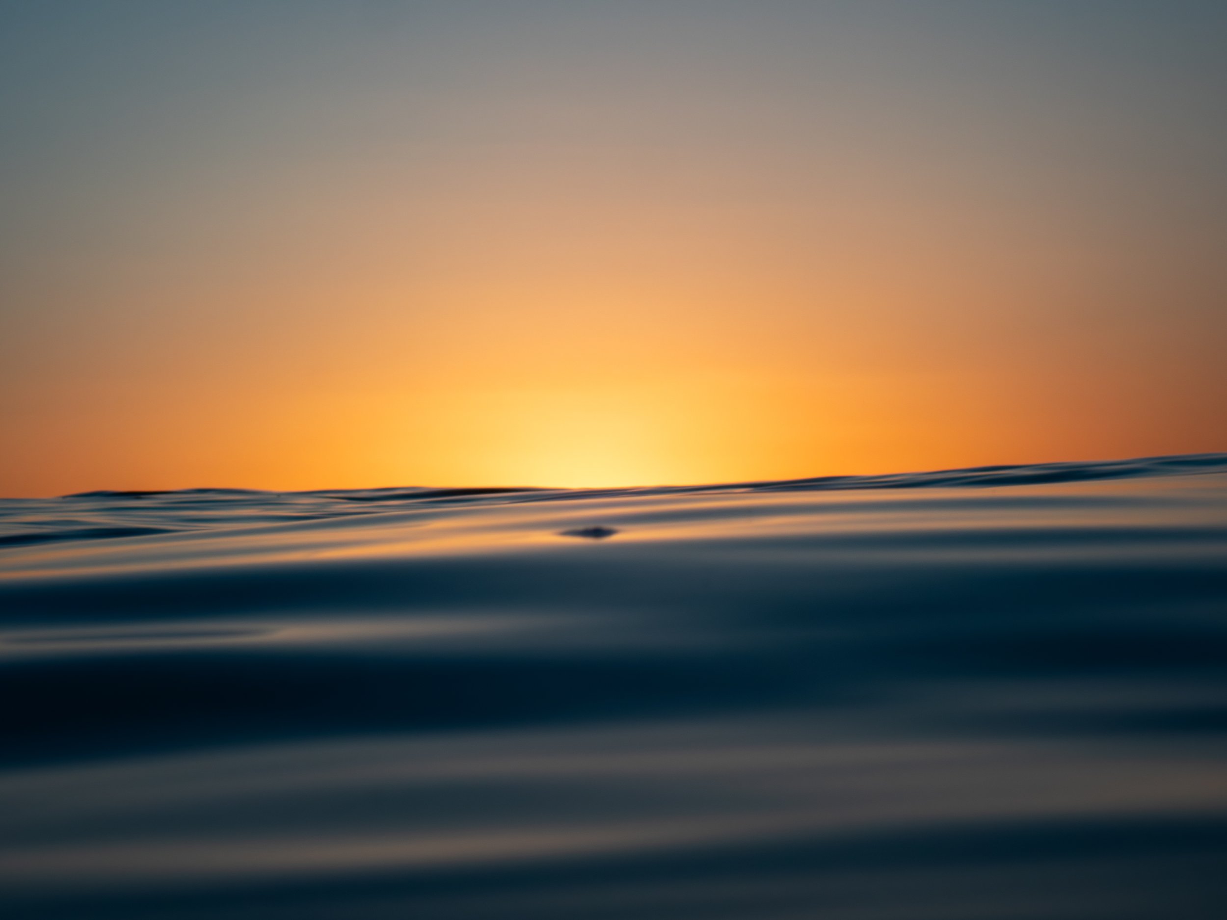 A calm ocean with gentle waves at sunset or sunrise with a colorful sky transitioning from blue to orange.