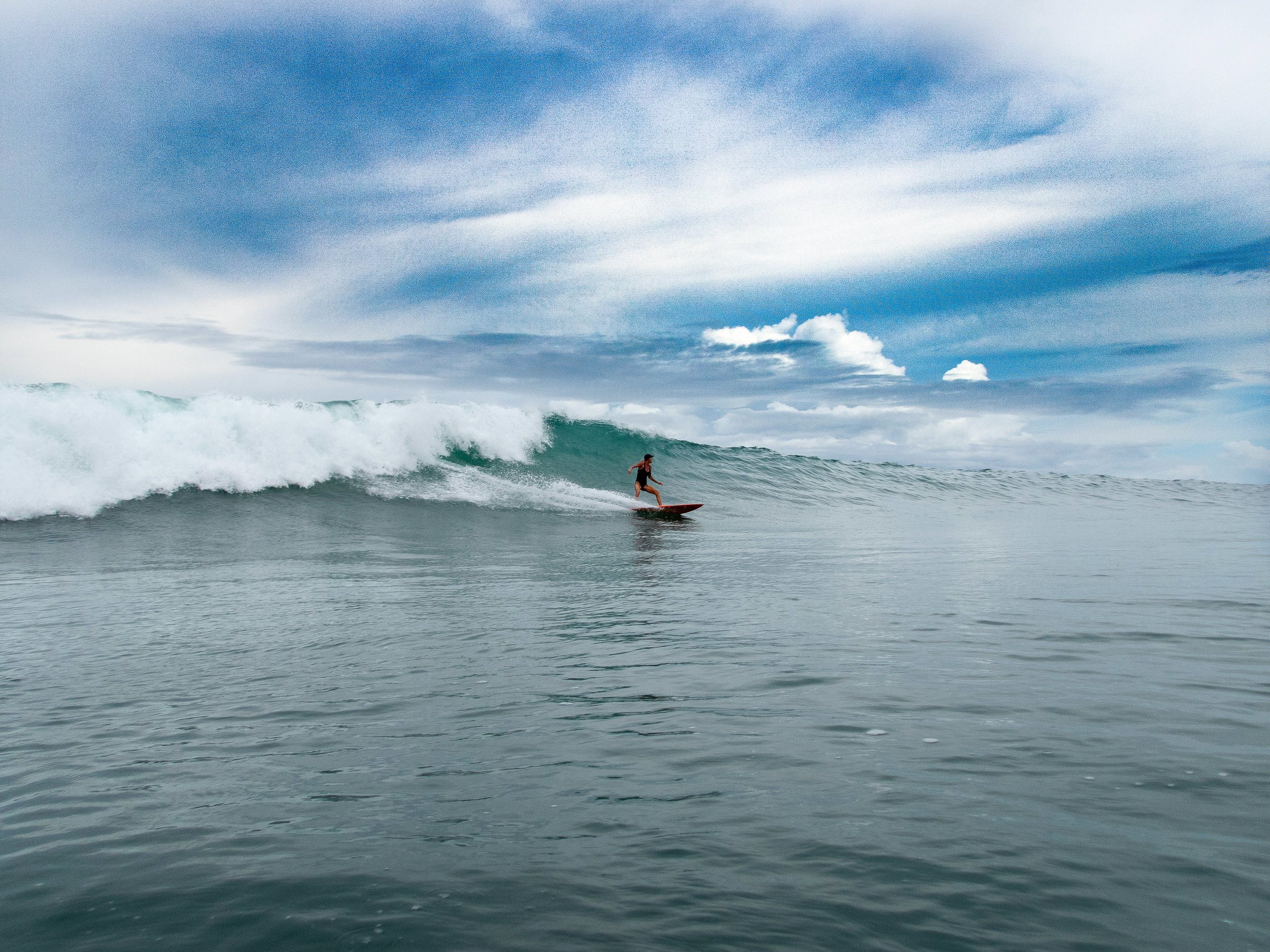 Person surfing on a large wave under a blue sky.