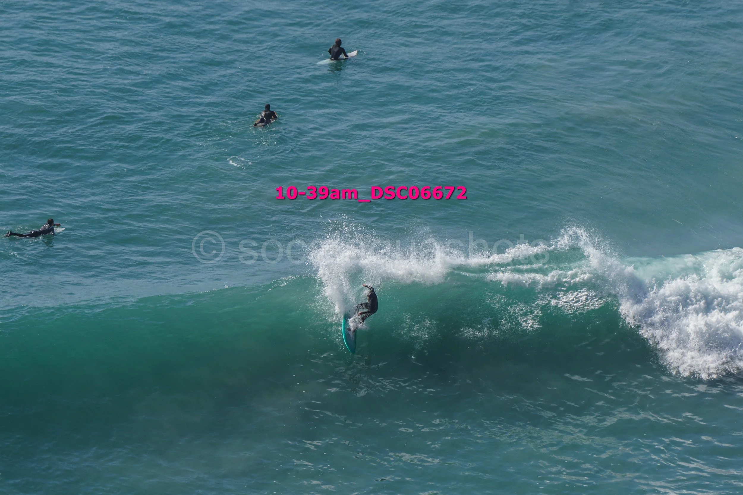 Surfer riding a wave in the ocean with three people swimming nearby.