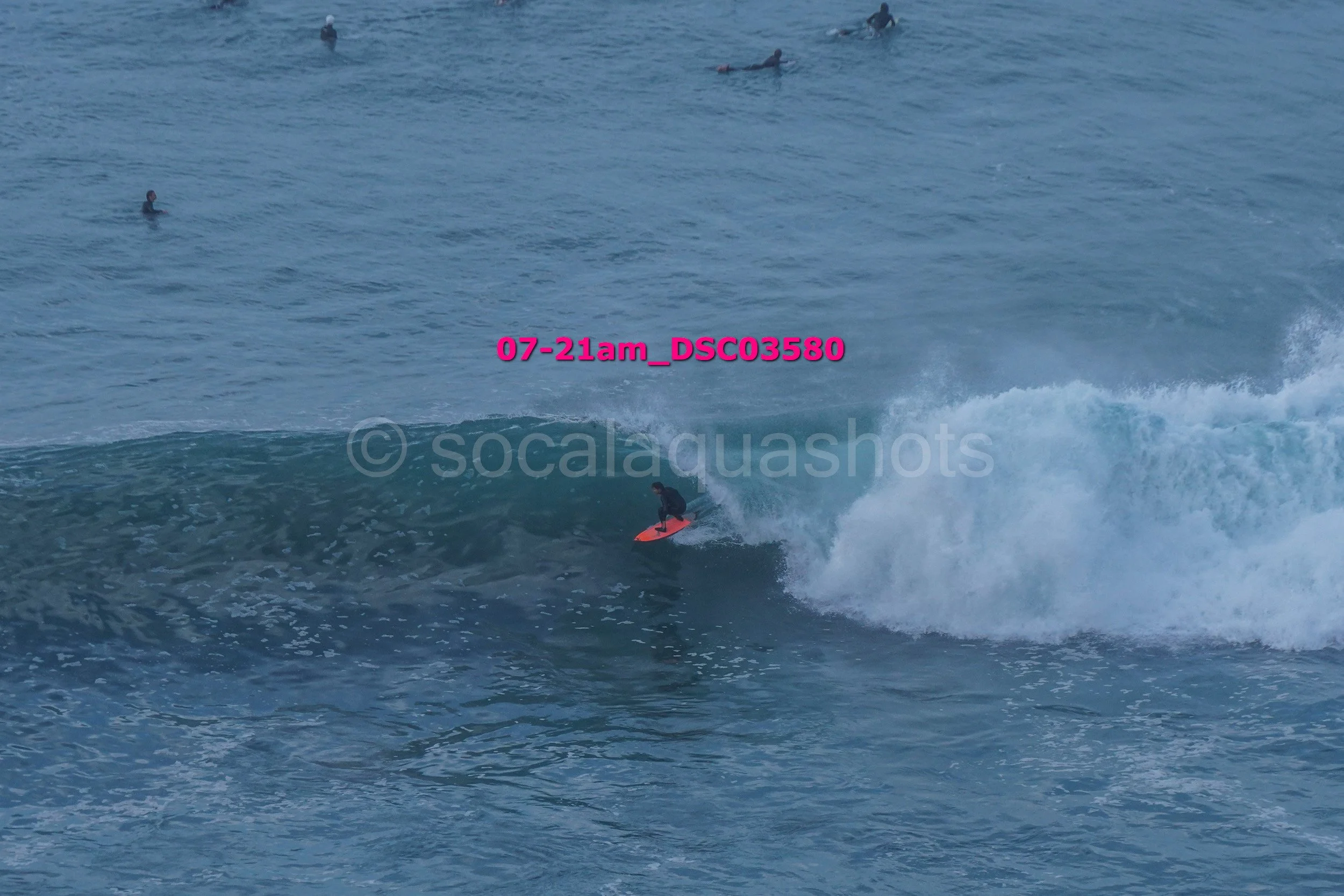 Surfer riding a wave in the ocean with several other swimmers floating in the background.