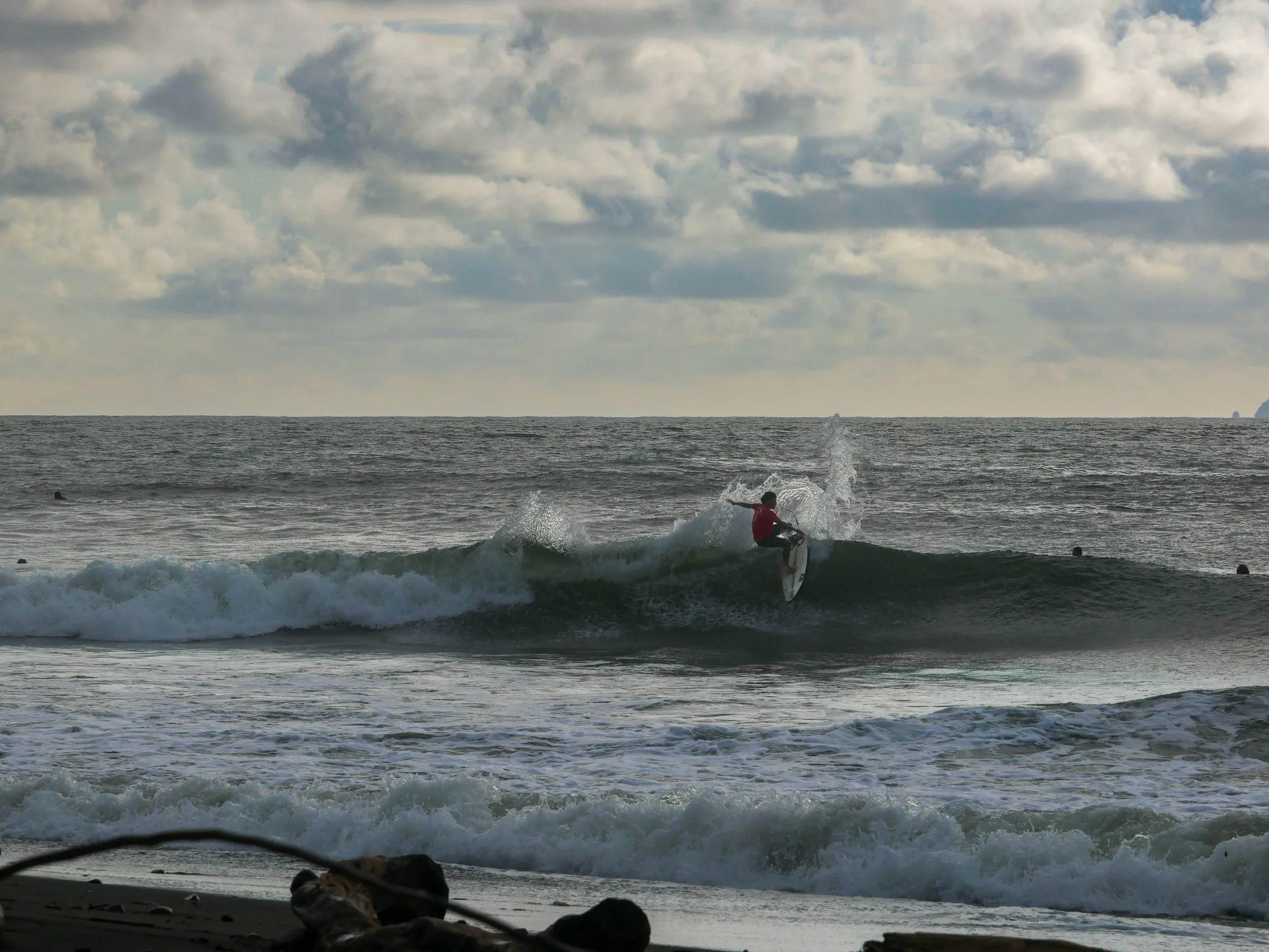 Surfer riding a wave on the ocean under cloudy skies at a beach.