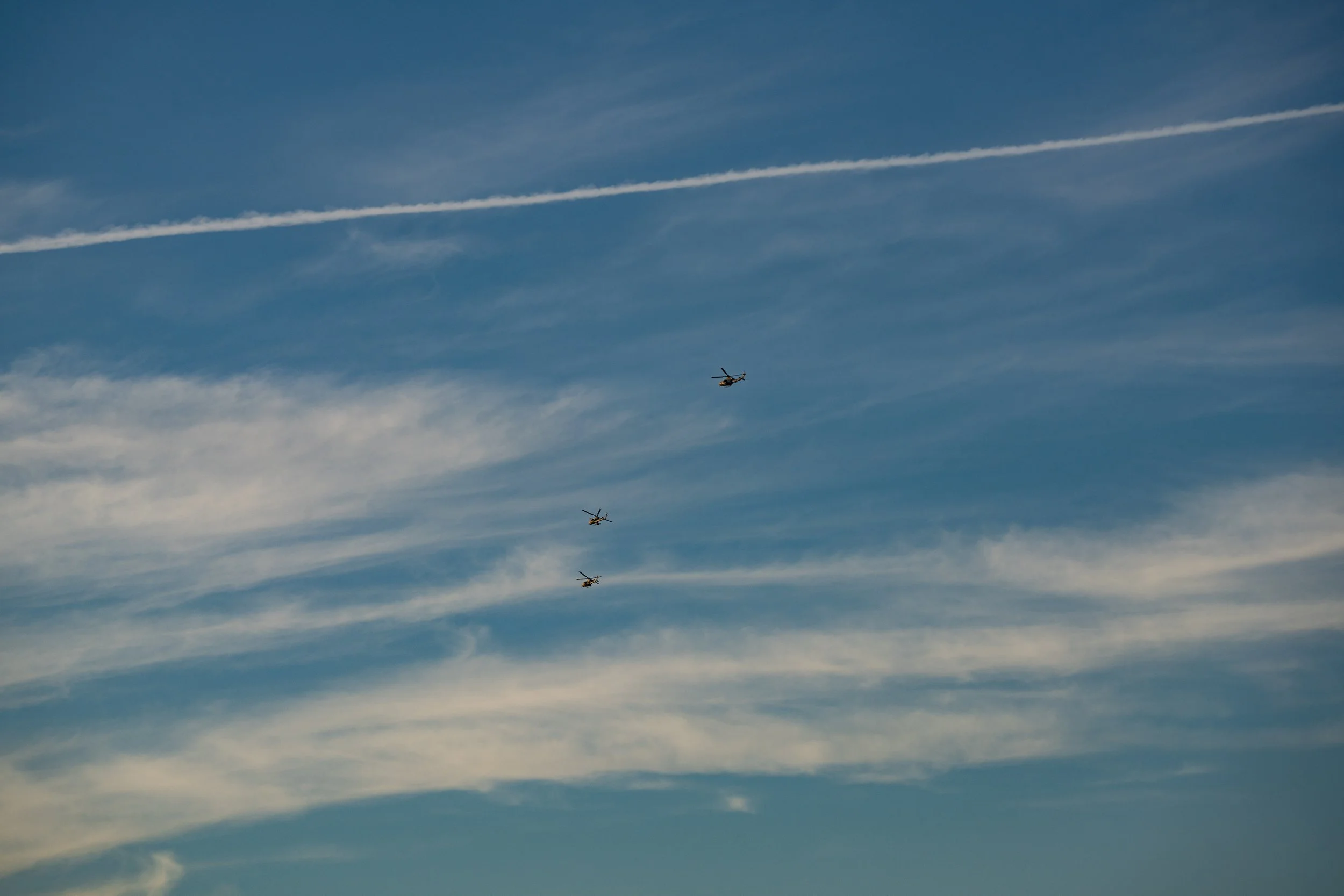 Three helicopters flying in formation against a blue sky with contrails.