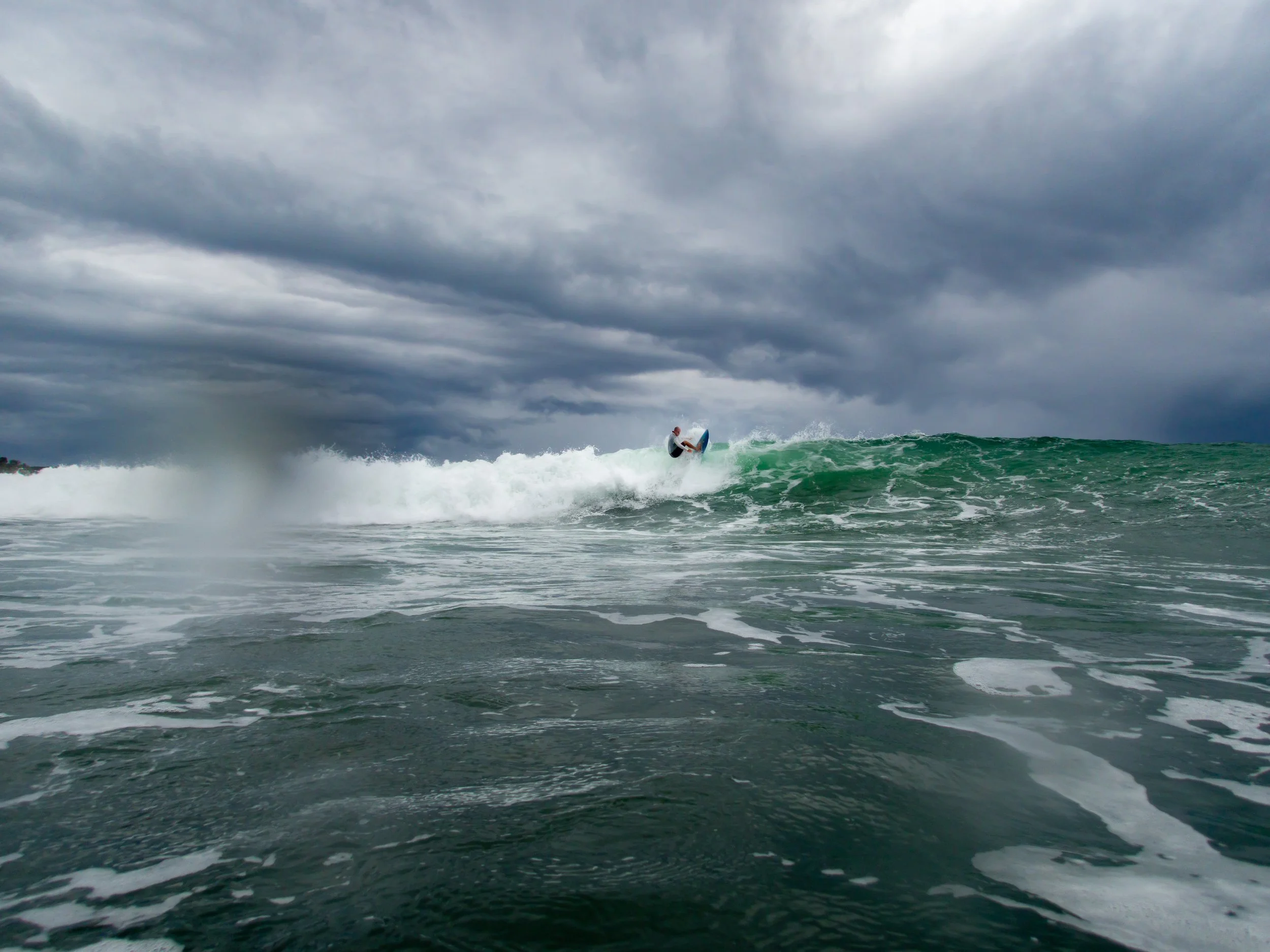 Surfer riding a wave under cloudy sky