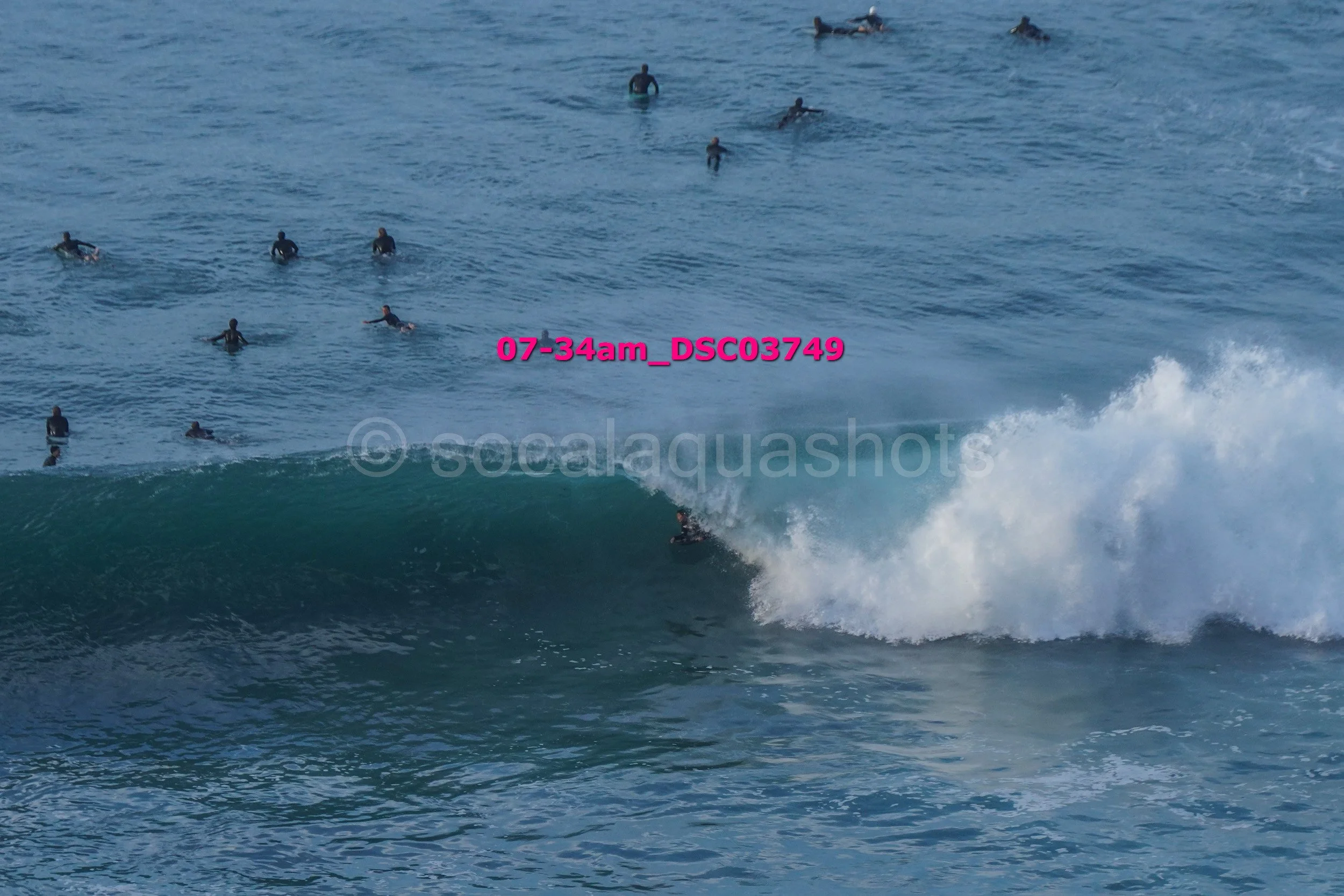 Surfer riding a wave with multiple people swimming in the ocean in the background.