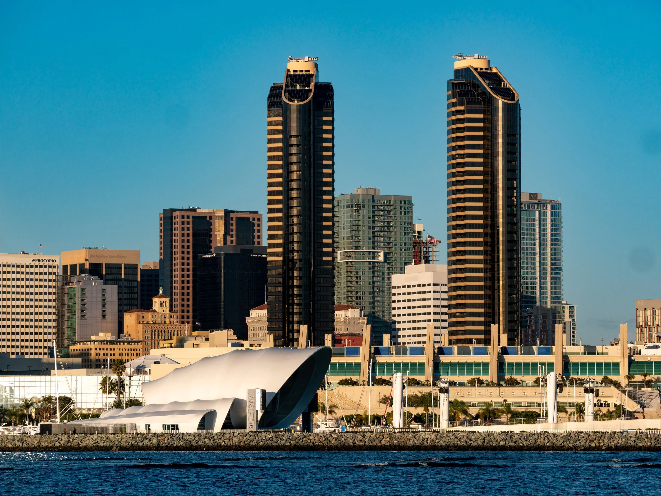 Skyline of downtown San Diego with modern skyscrapers seen from across the water, including the distinctive white Seaport Village building in the foreground.