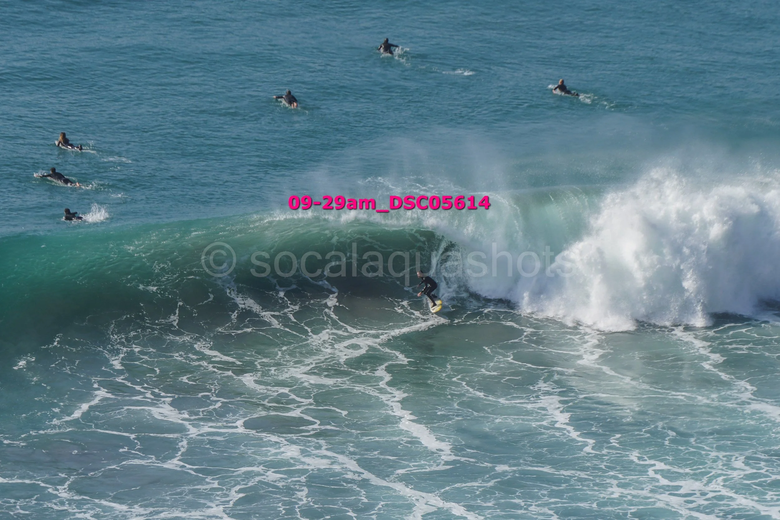 Surfer riding a large wave with several people in the water behind him.