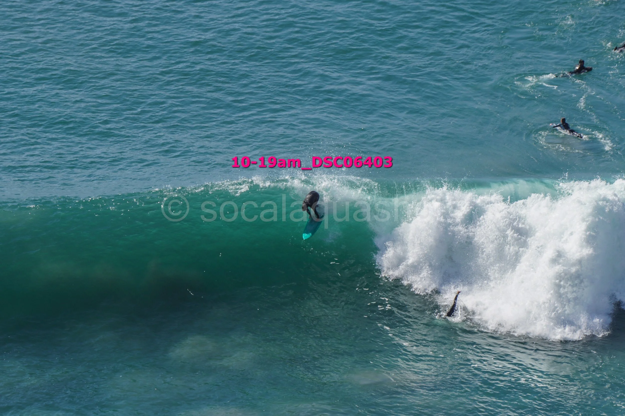 Surfer falling off a surfboard on a large ocean wave with three other surfers in the background.